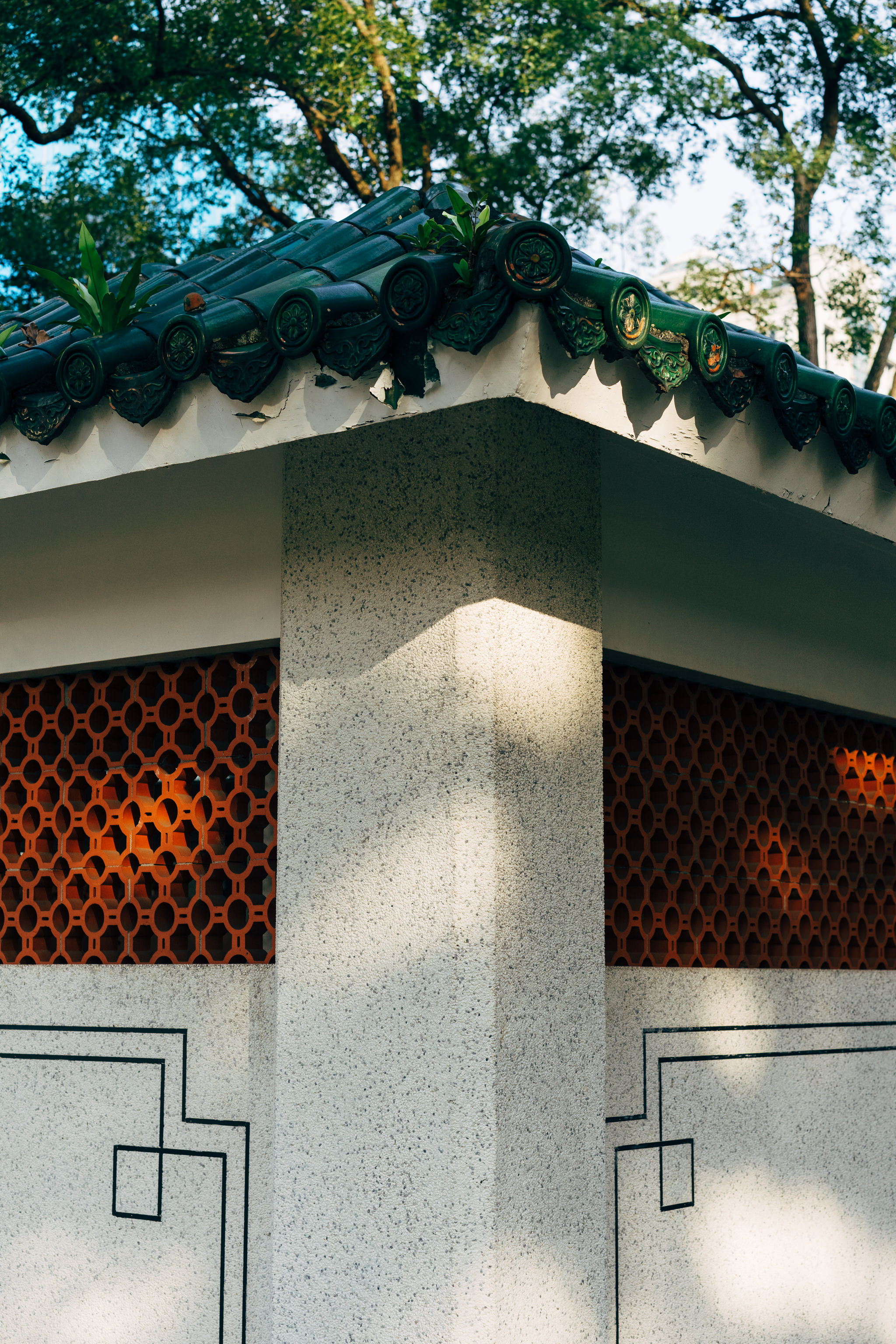 Close-up of a corner of a light-grey building with a dark-green roof, featuring orange lattice-like panels.