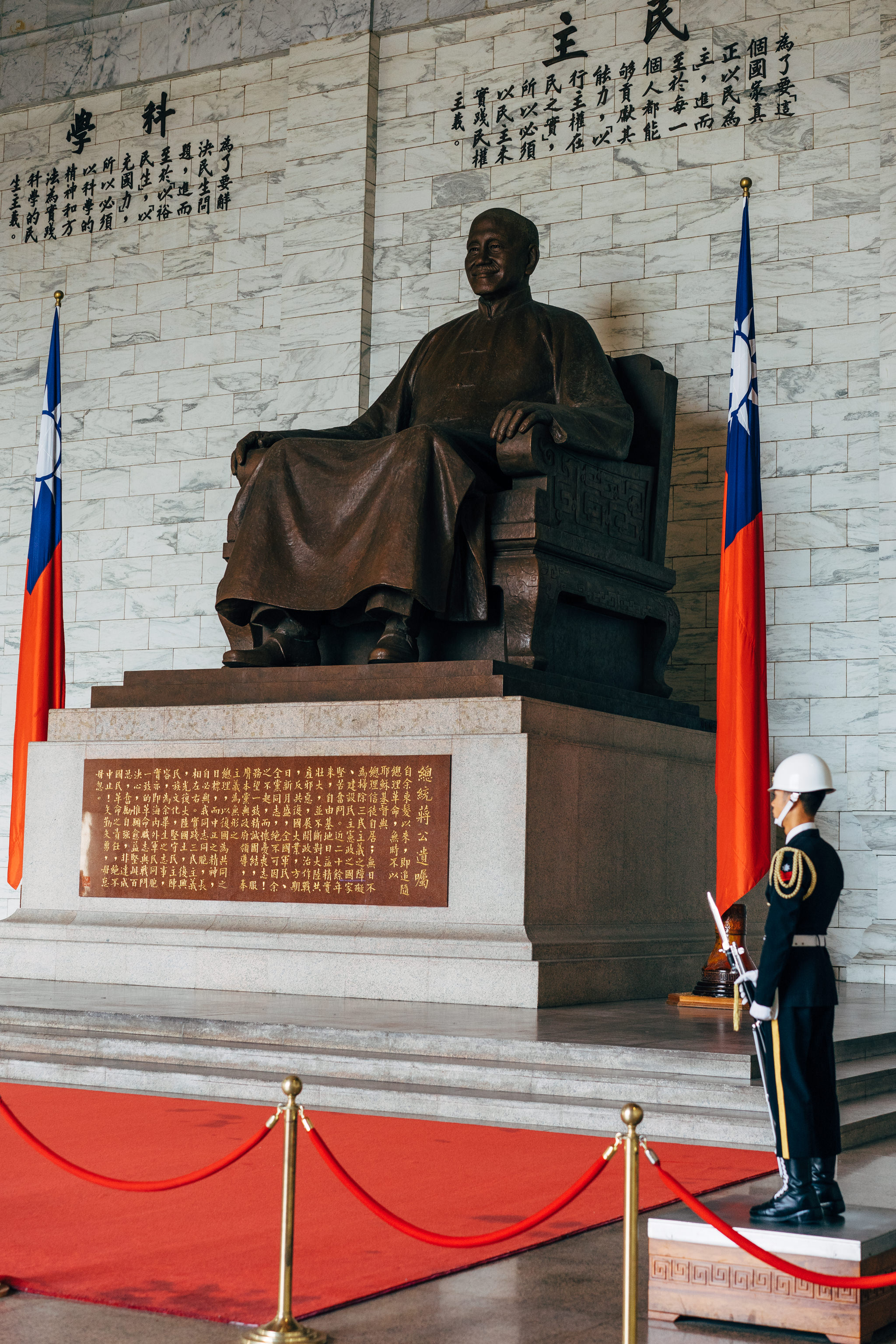 Large bronze statue of Chiang Kai-shek seated on a throne, flanked by Taiwanese flags, with a guard standing at attention.