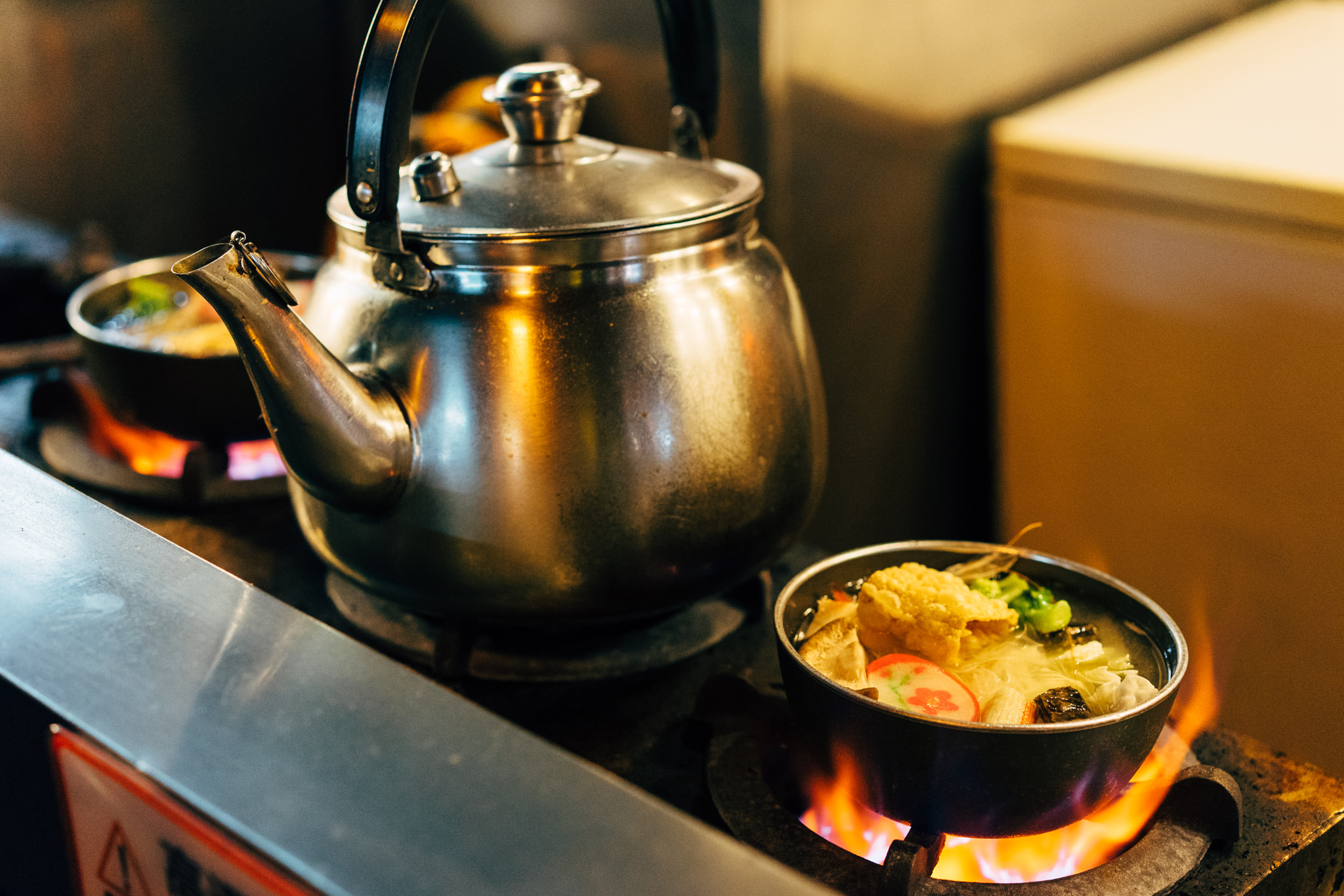 Street food cooking scene with a kettle and a bowl of stew over open flames.