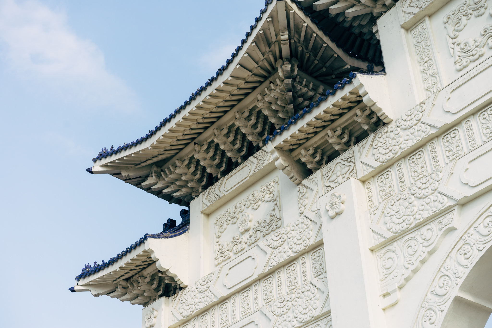 Close-up of ornate white archway with blue-tiled roof against a blue sky.