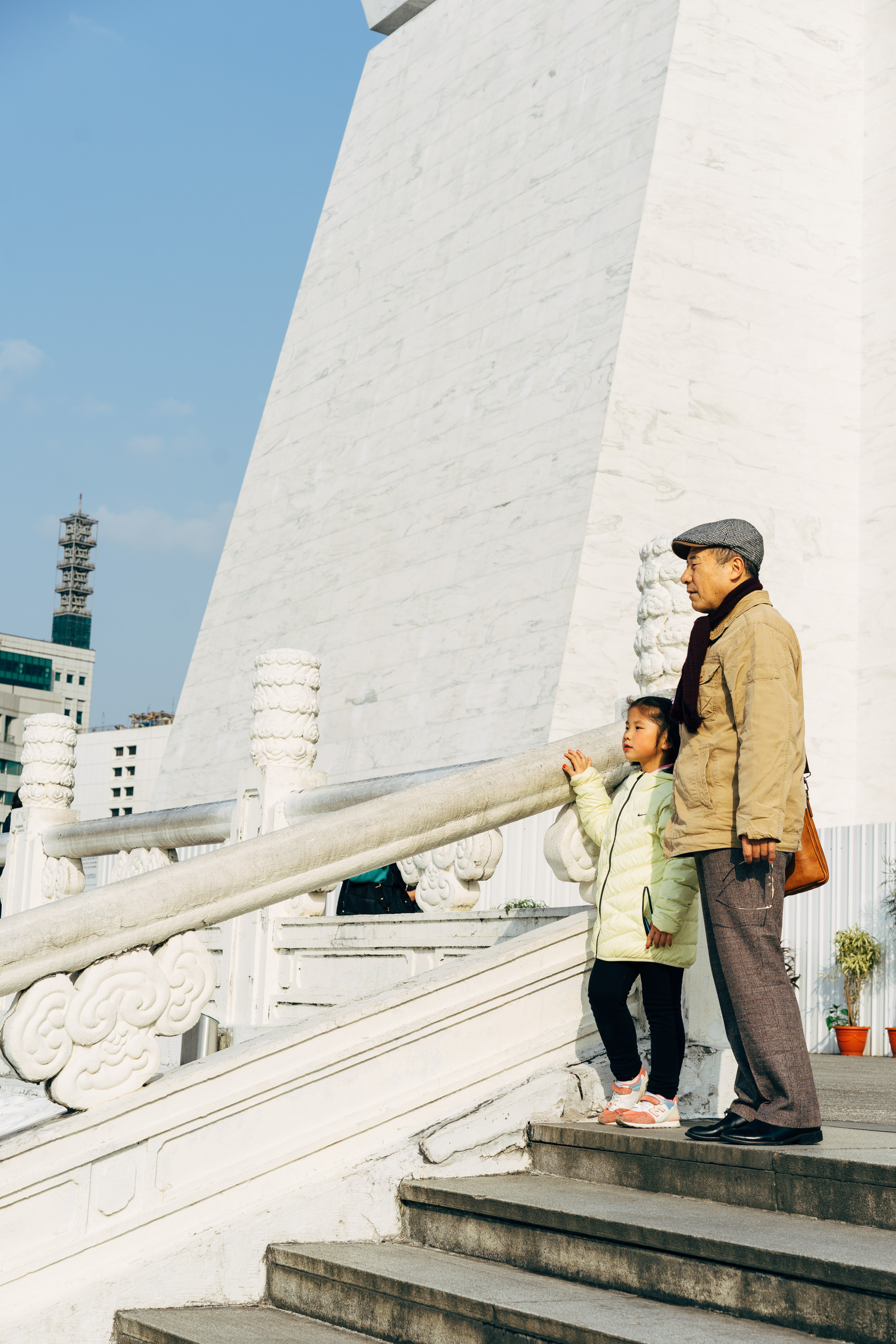 Grandfather and granddaughter stand on steps at a white marble monument in Taiwan.