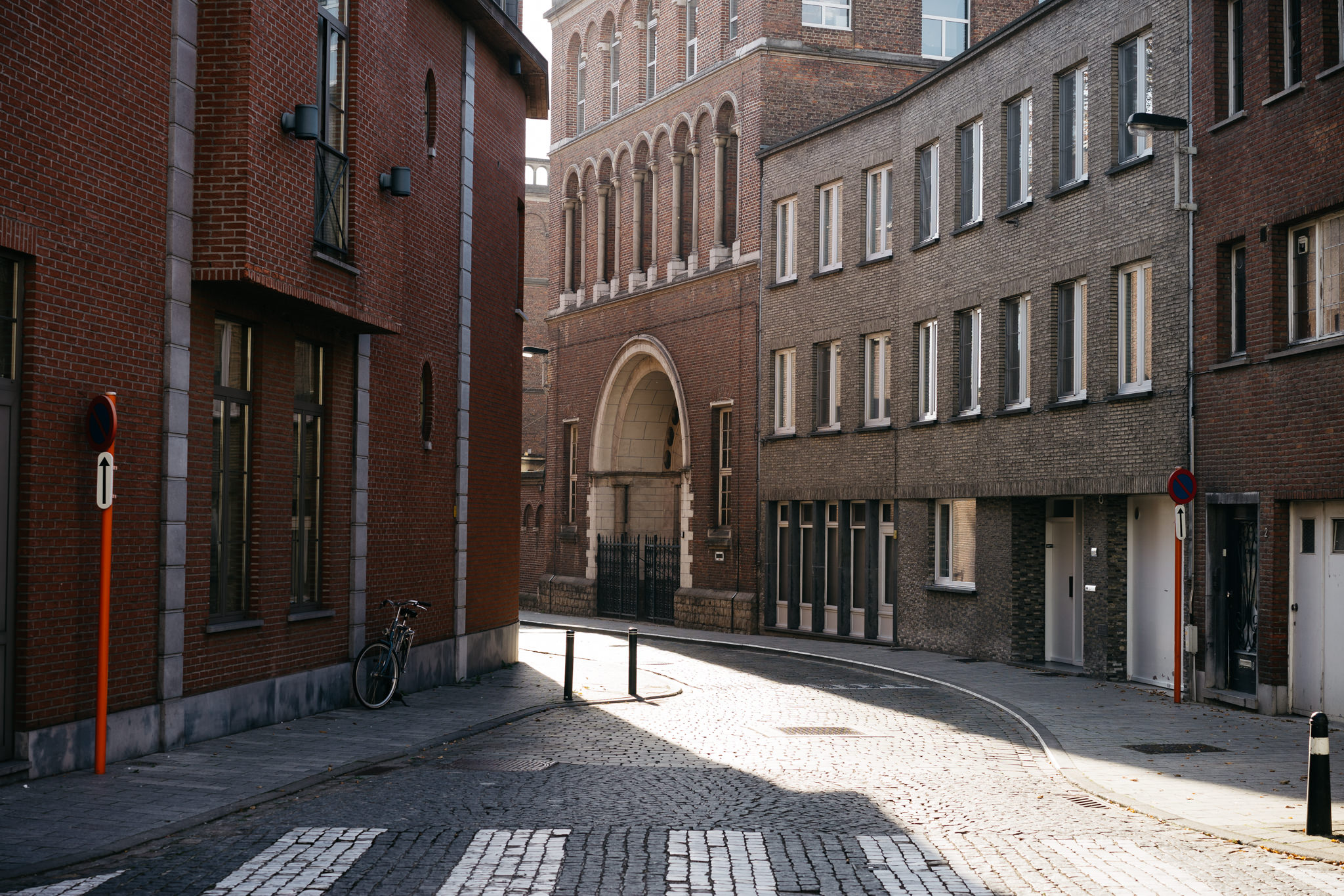 Sunlit cobblestone street in Lier, Belgium, between brick buildings.