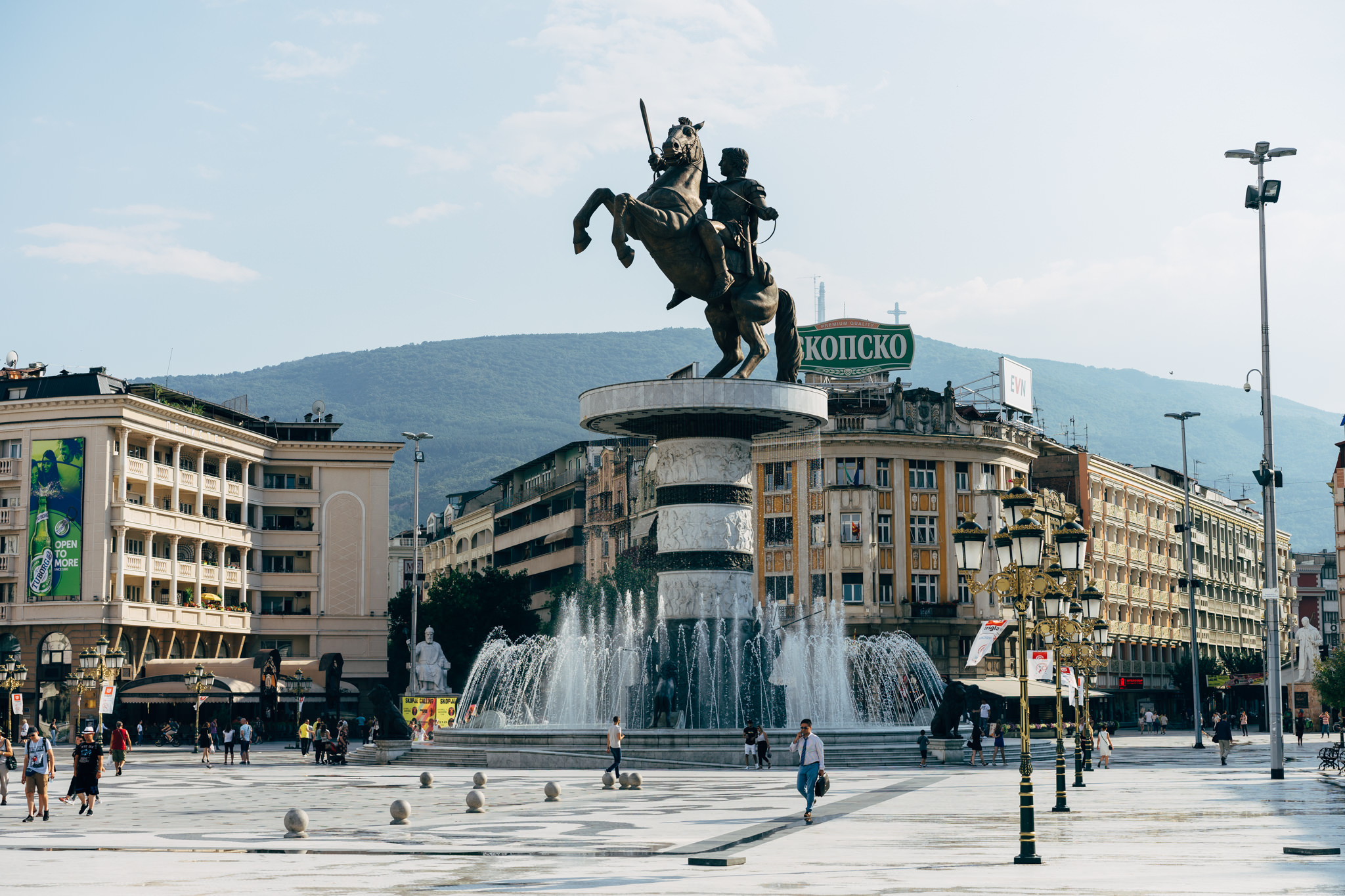 A bronze equestrian statue in Skopje's Macedonia Square, with a fountain and surrounding buildings.