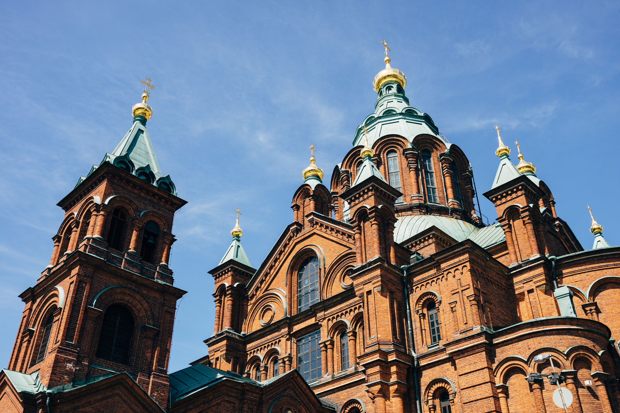 Low-angle view of Uspenski Cathedral in Helsinki, showcasing its red brick facade, green domes, and golden crosses.