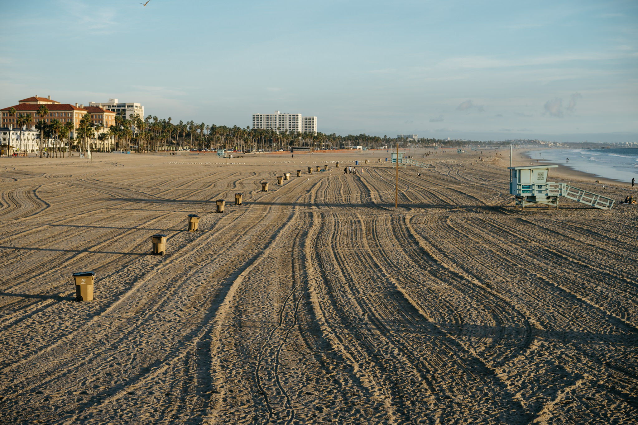 California beach with tire tracks in the sand, buildings in the background, and a lifeguard station.
