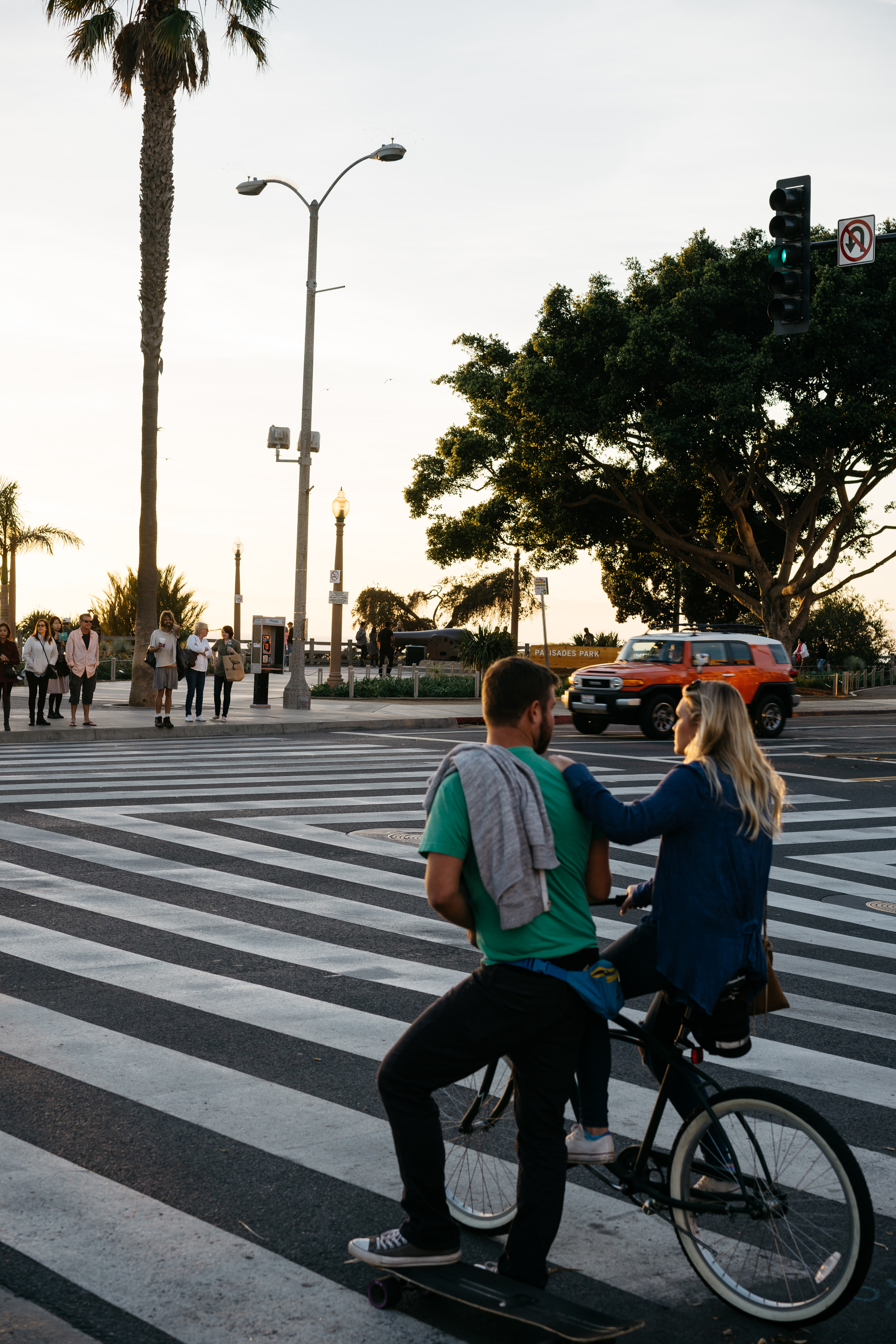 Couple on bike and skateboard crossing a crosswalk at sunset in California.