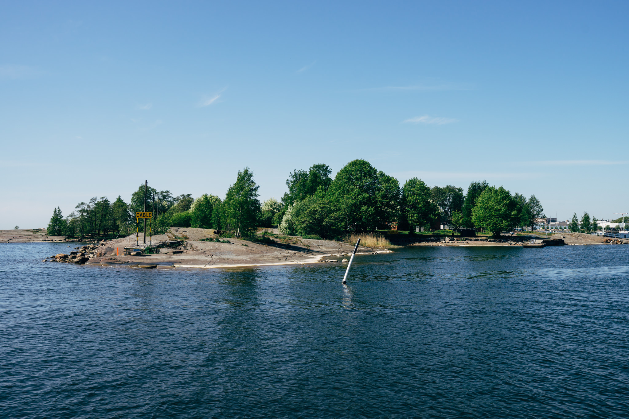 Helsinki island with trees under a clear blue sky.