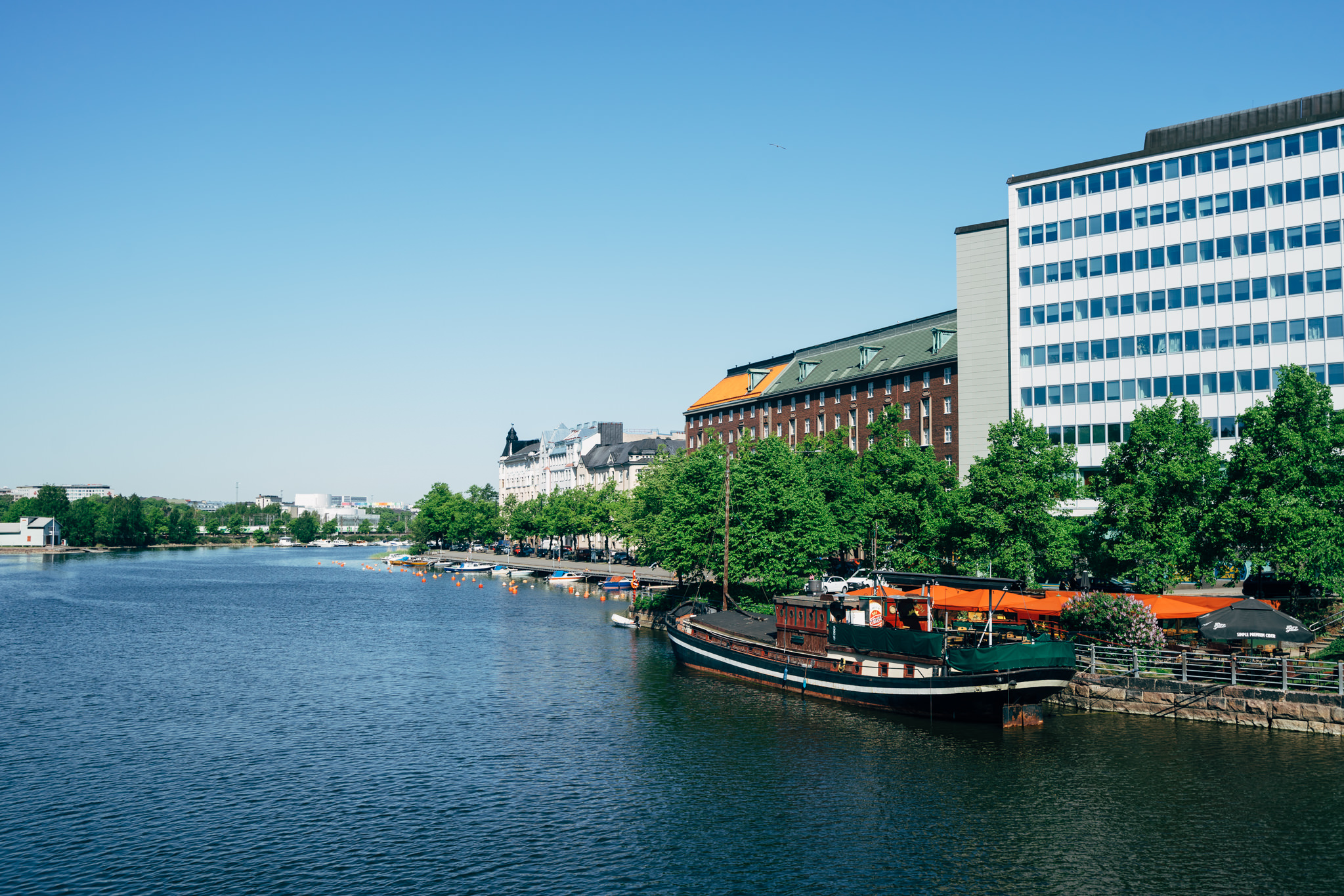Helsinki riverfront in summer with buildings and a boat.