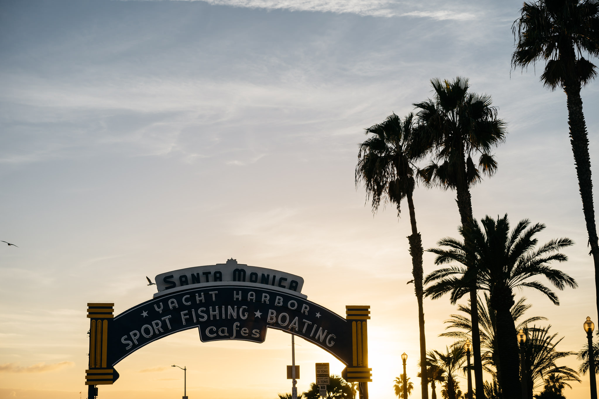 Santa Monica harbor entrance sign at sunset, silhouetted against palm trees.