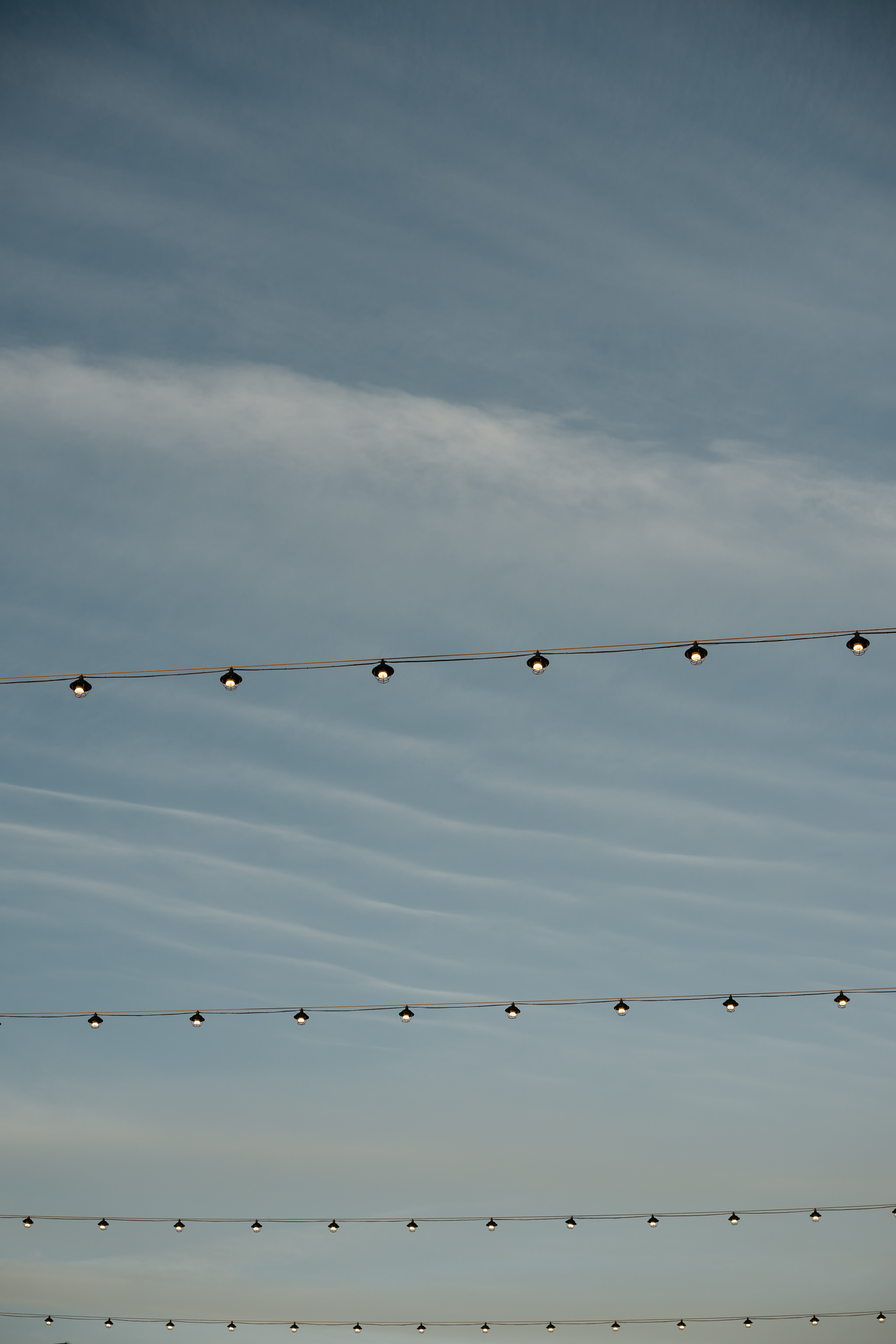 Three strings of outdoor lights against a twilight sky.