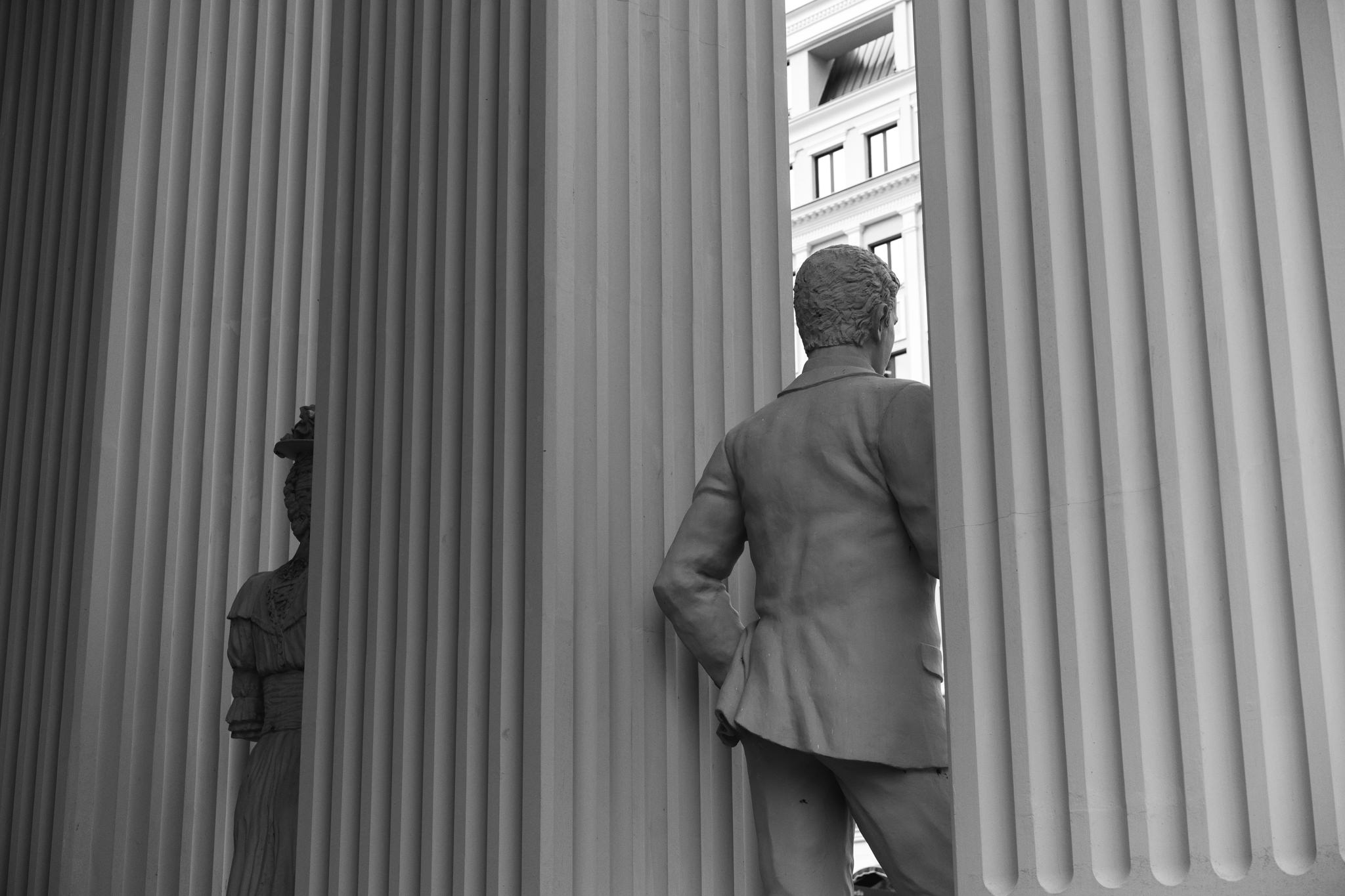 Black and white photo of two statues partially obscured by columns.