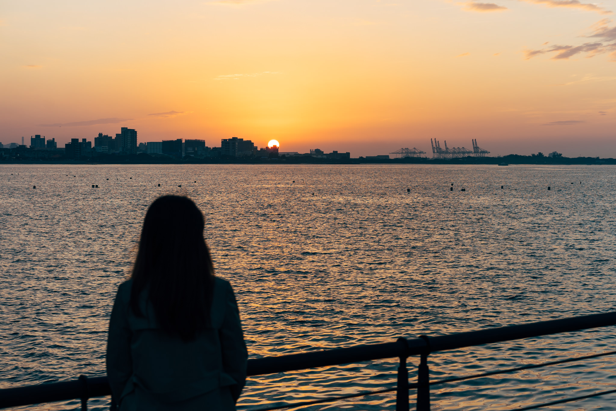 Silhouette of a person facing a sunset over water with a city skyline in the distance.