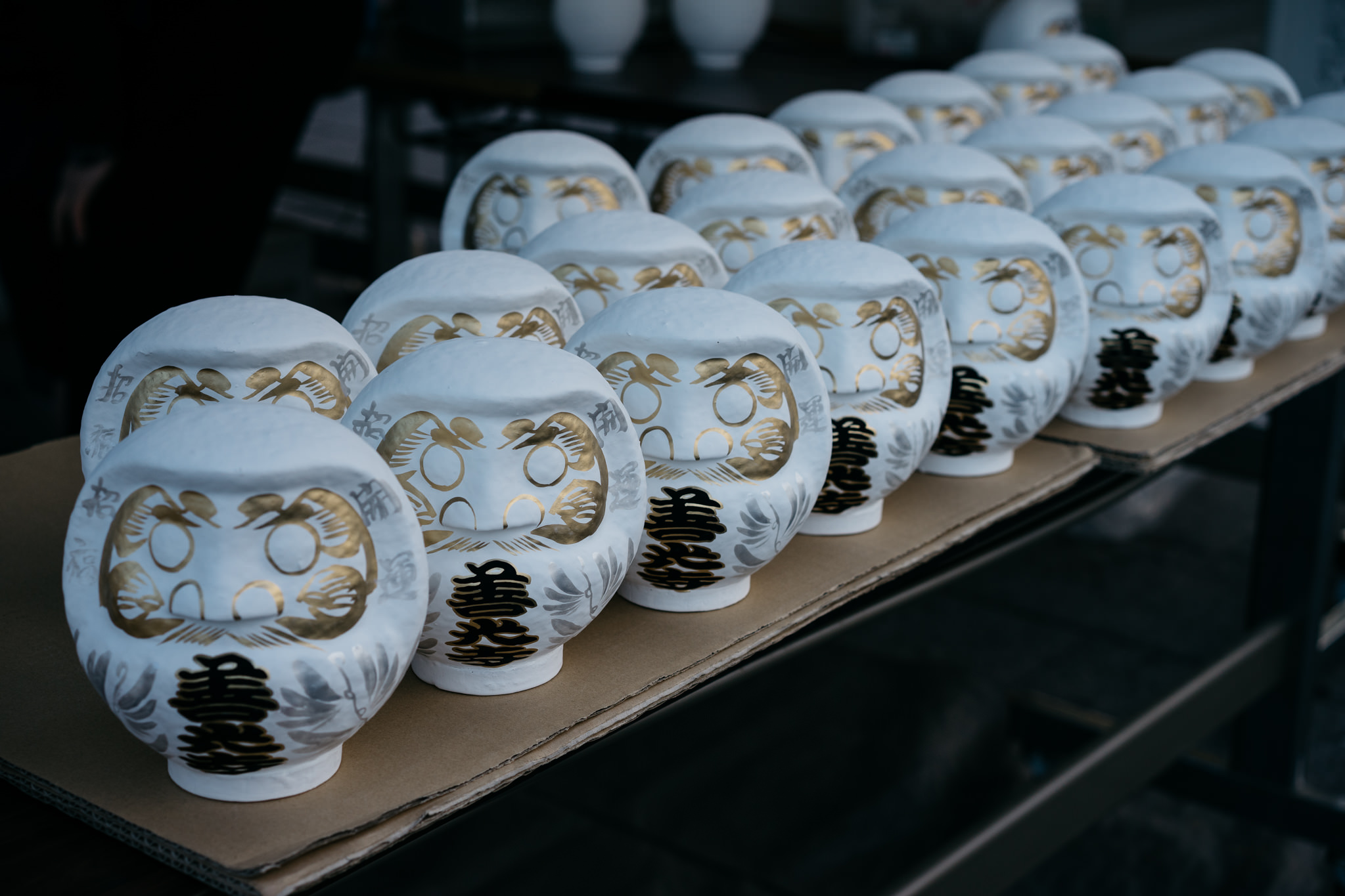 Row of white Daruma dolls with gold and black detailing at Zenko-ji Temple.