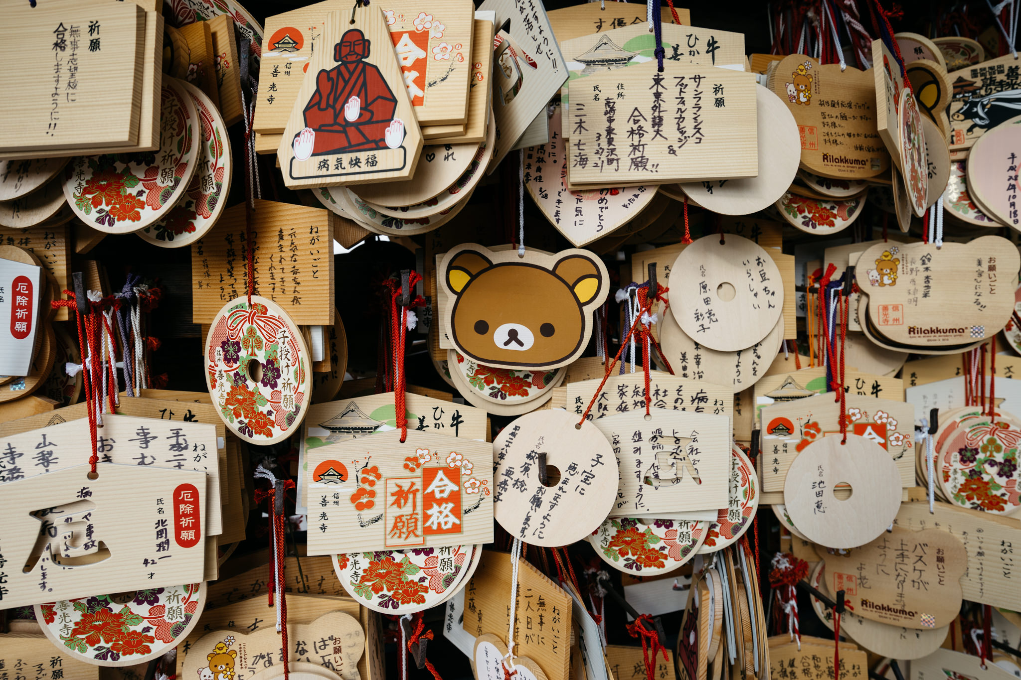 Close-up of numerous ema (wooden plaques) hanging at Zenko-ji Temple, featuring various designs and prayers written in Japanese.