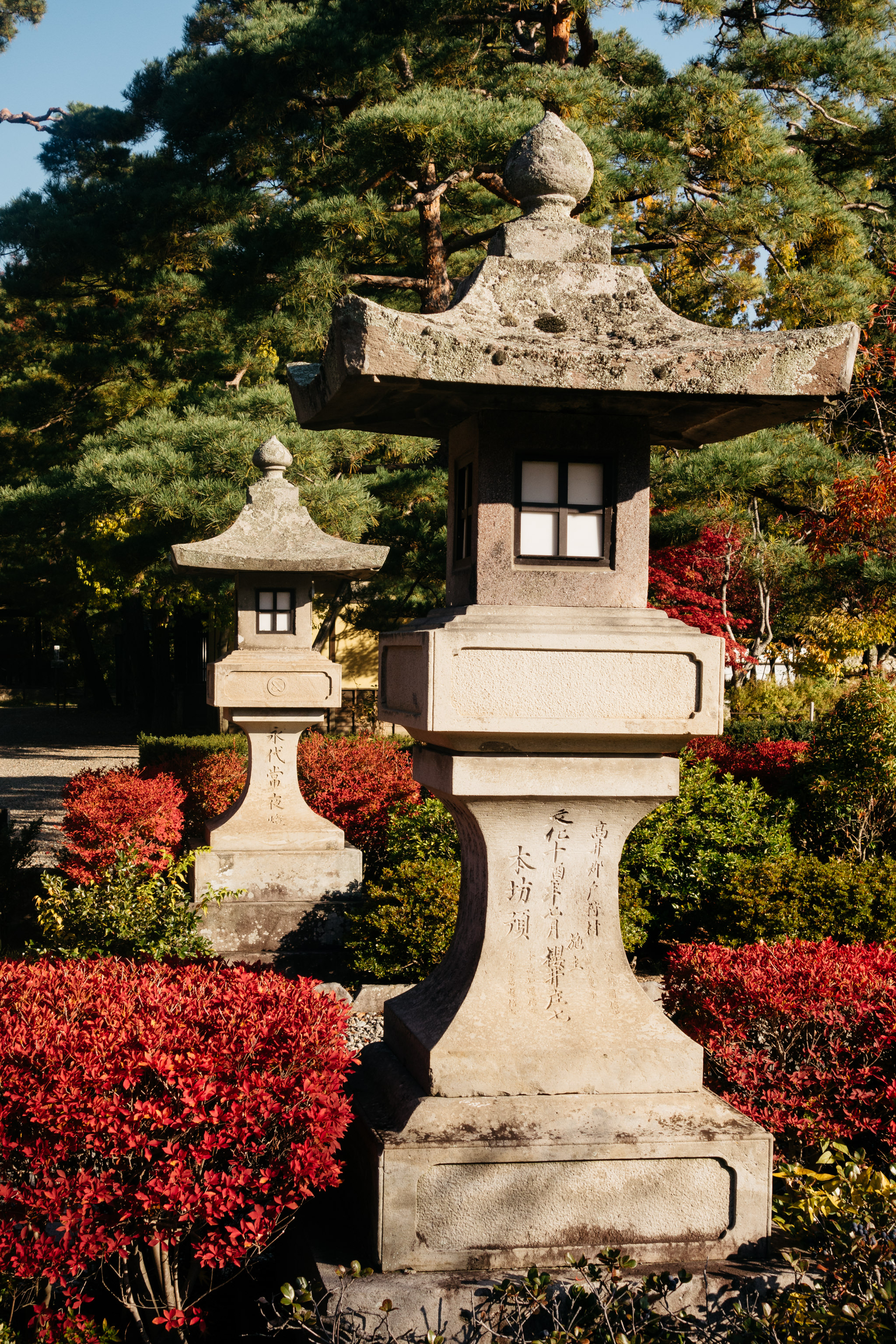 Two stone lanterns in a Zenko-ji garden with red foliage.