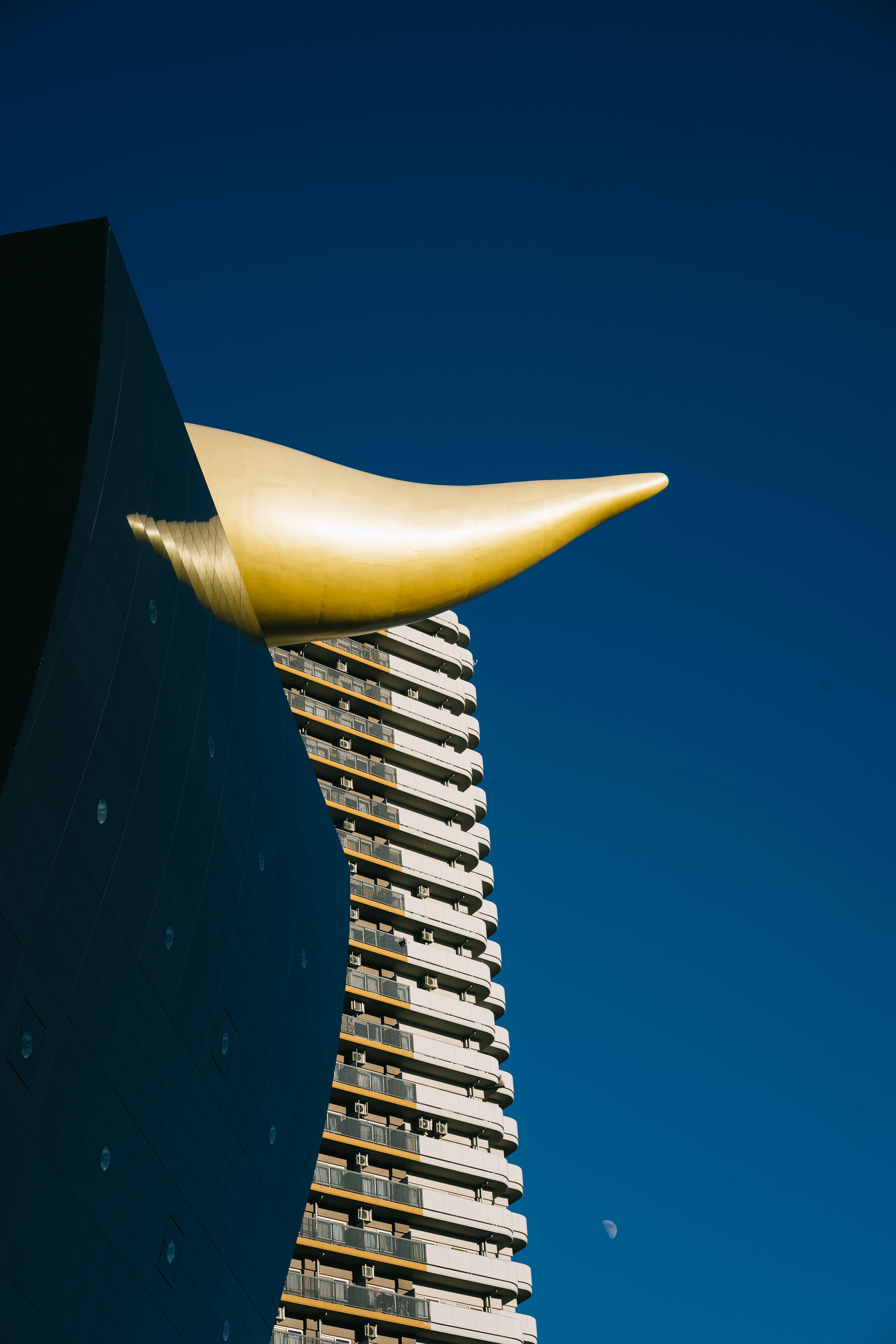 Low-angle view of a gold horn-shaped structure against a blue sky, with a multi-story building partially visible behind it.