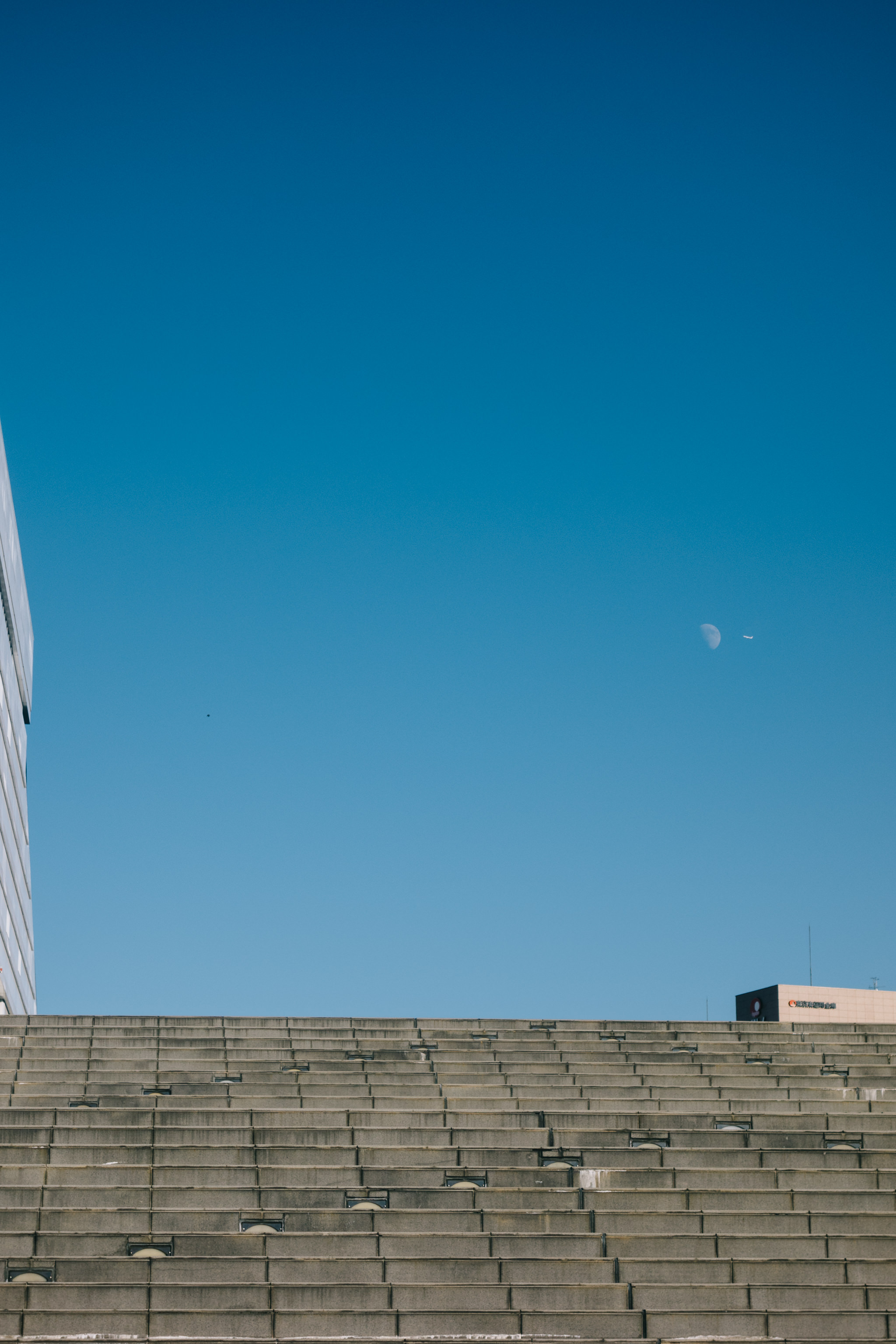 Concrete stairs under a clear blue sky with a sliver of moon visible.