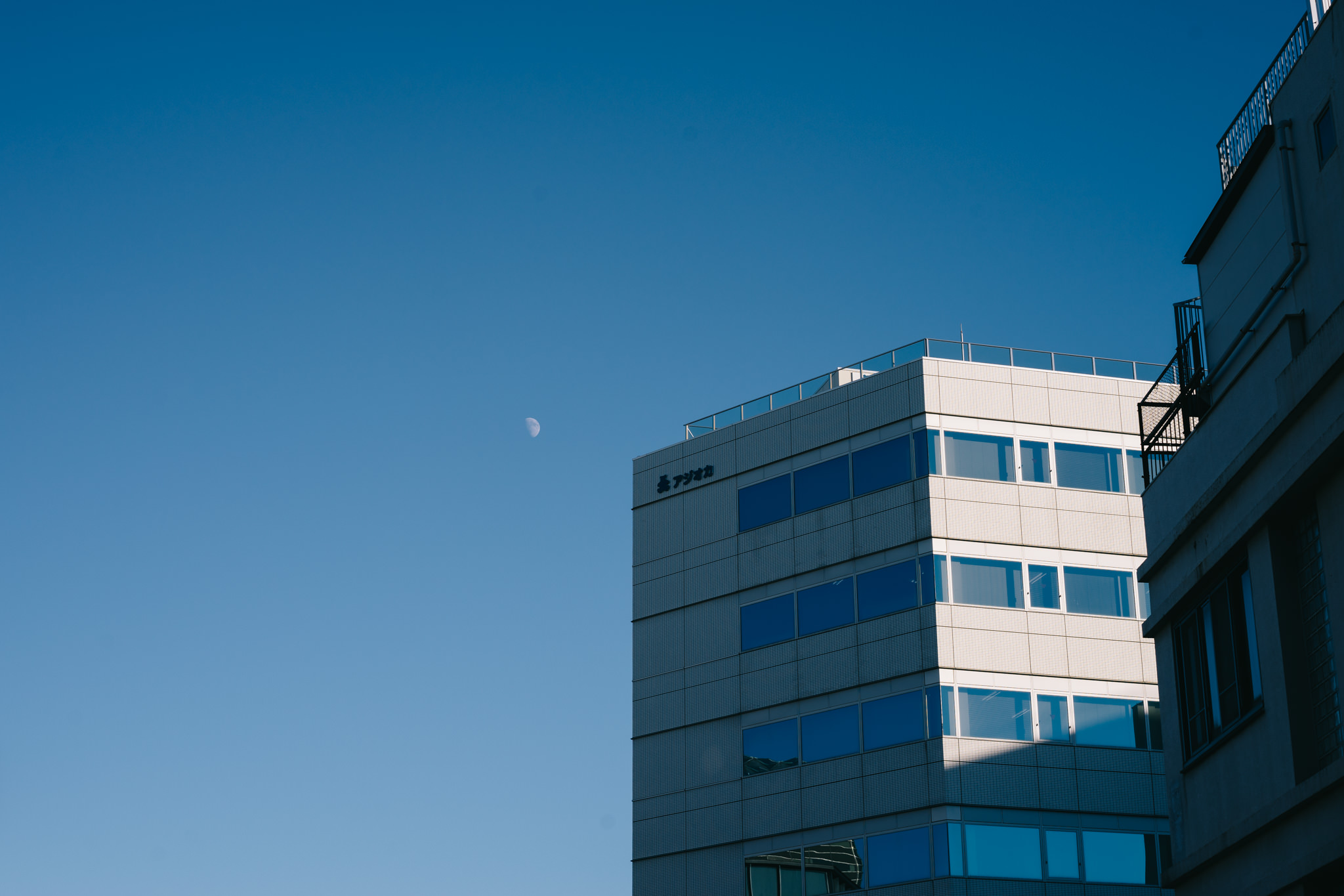 Crescent moon in a clear blue sky above a Tokyo building.