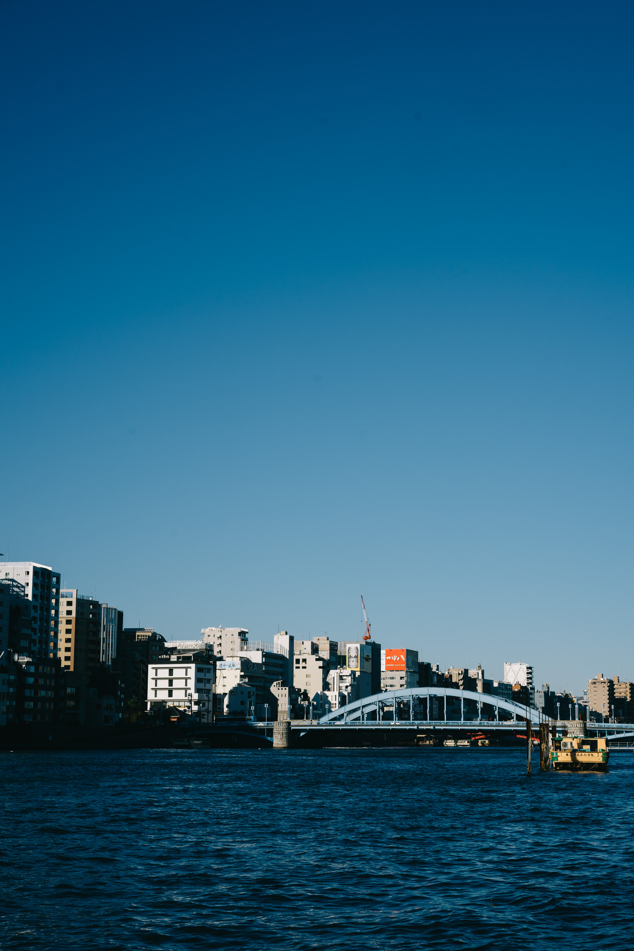 Tokyo cityscape with bridge over river under a clear blue sky.
