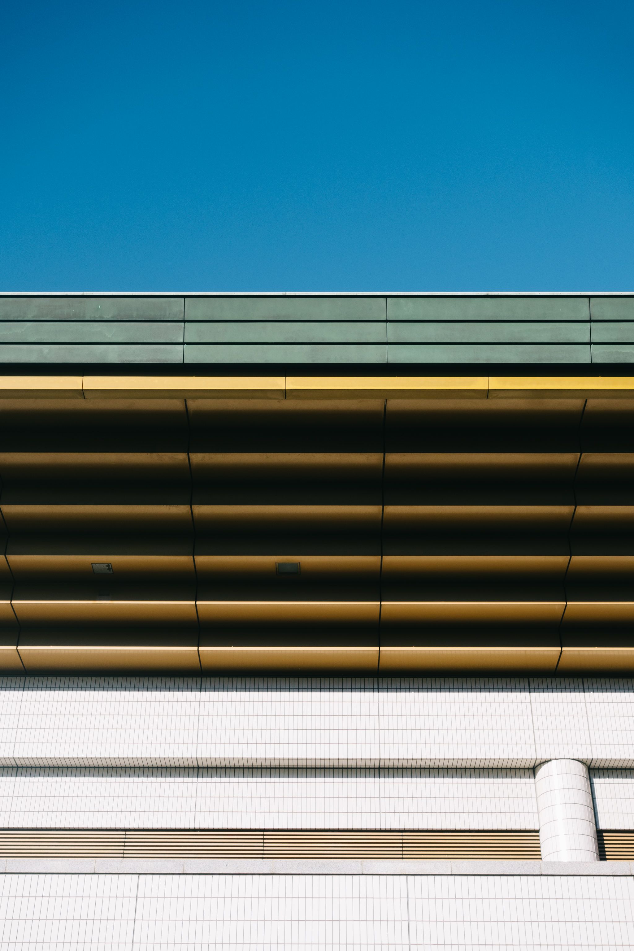 Abstract image of building exterior with teal, gold, and white architectural details against a blue sky.