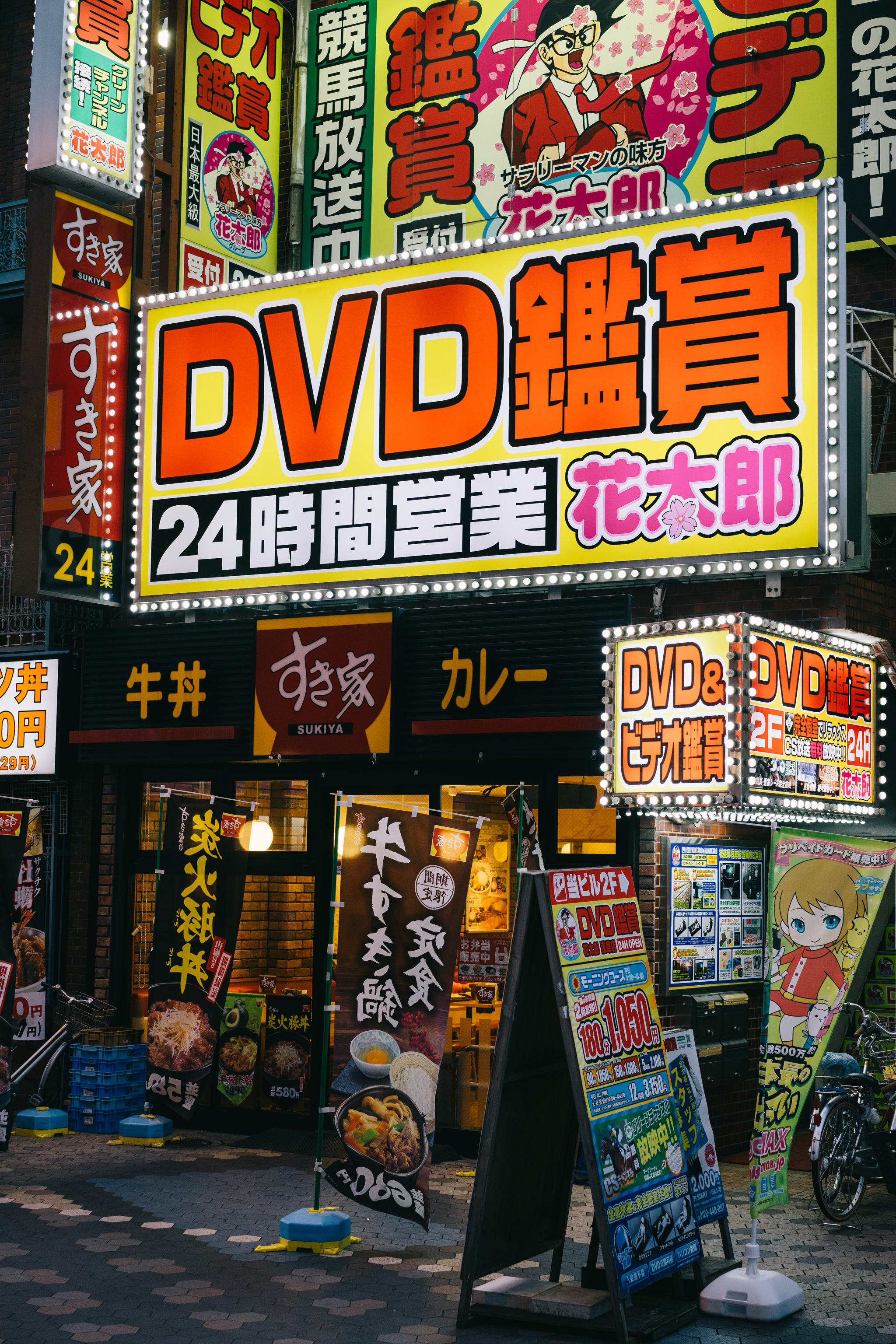 Tokyo shop with brightly lit DVD rental signs in Japanese.