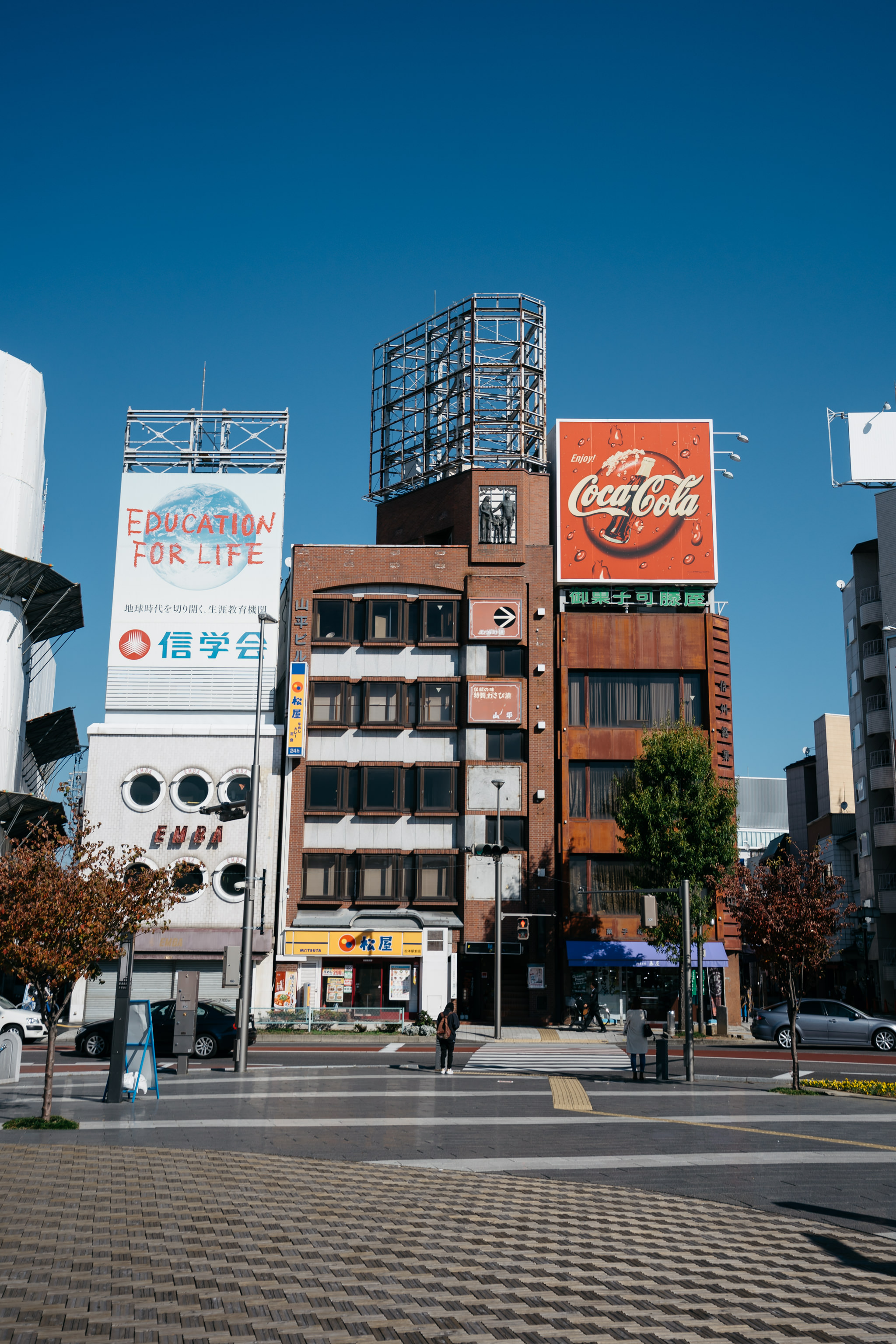 Matsumoto city street scene with buildings and billboards, including a Coca-Cola advertisement.