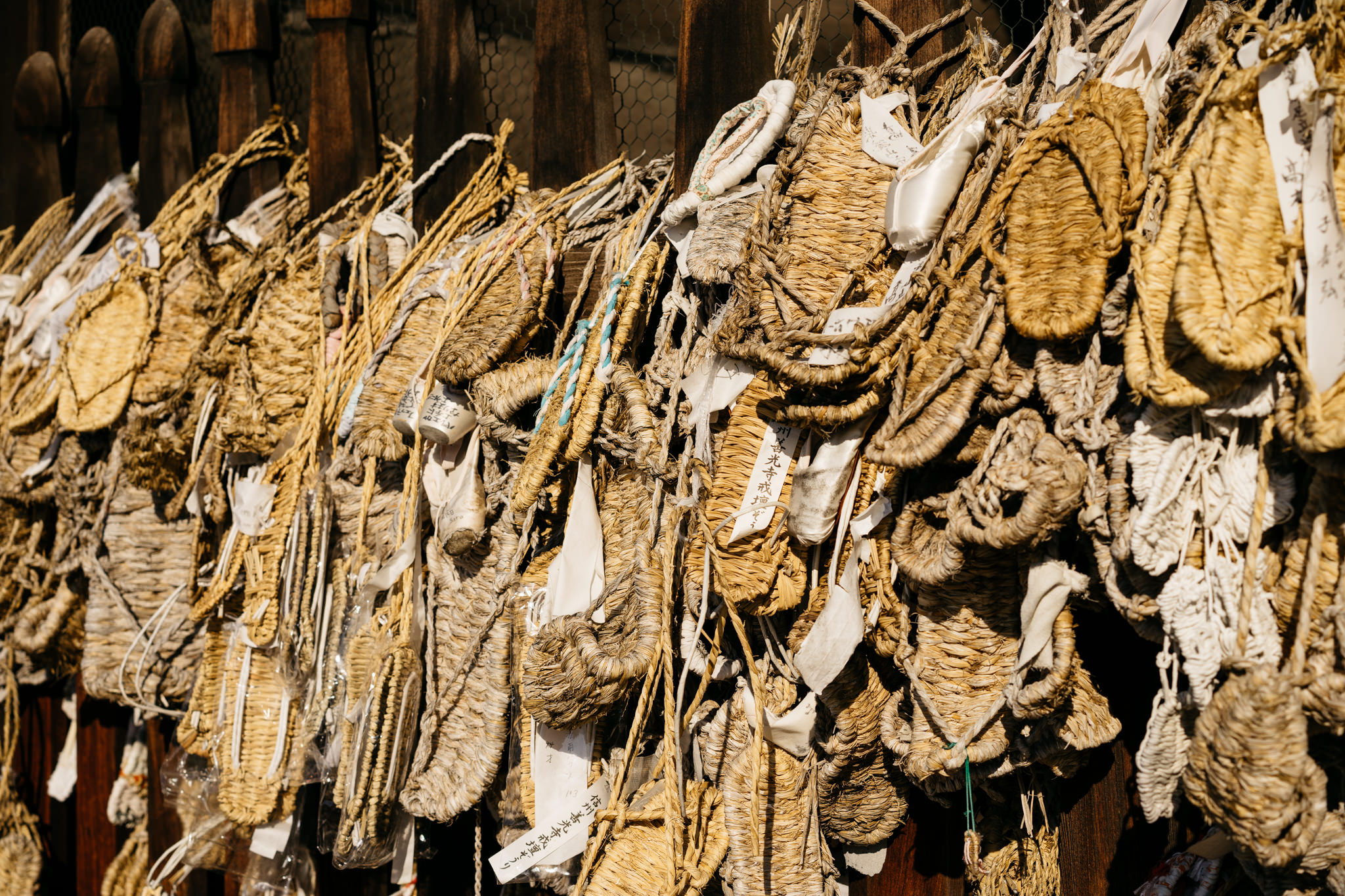 Many straw sandals hanging on a wooden fence.