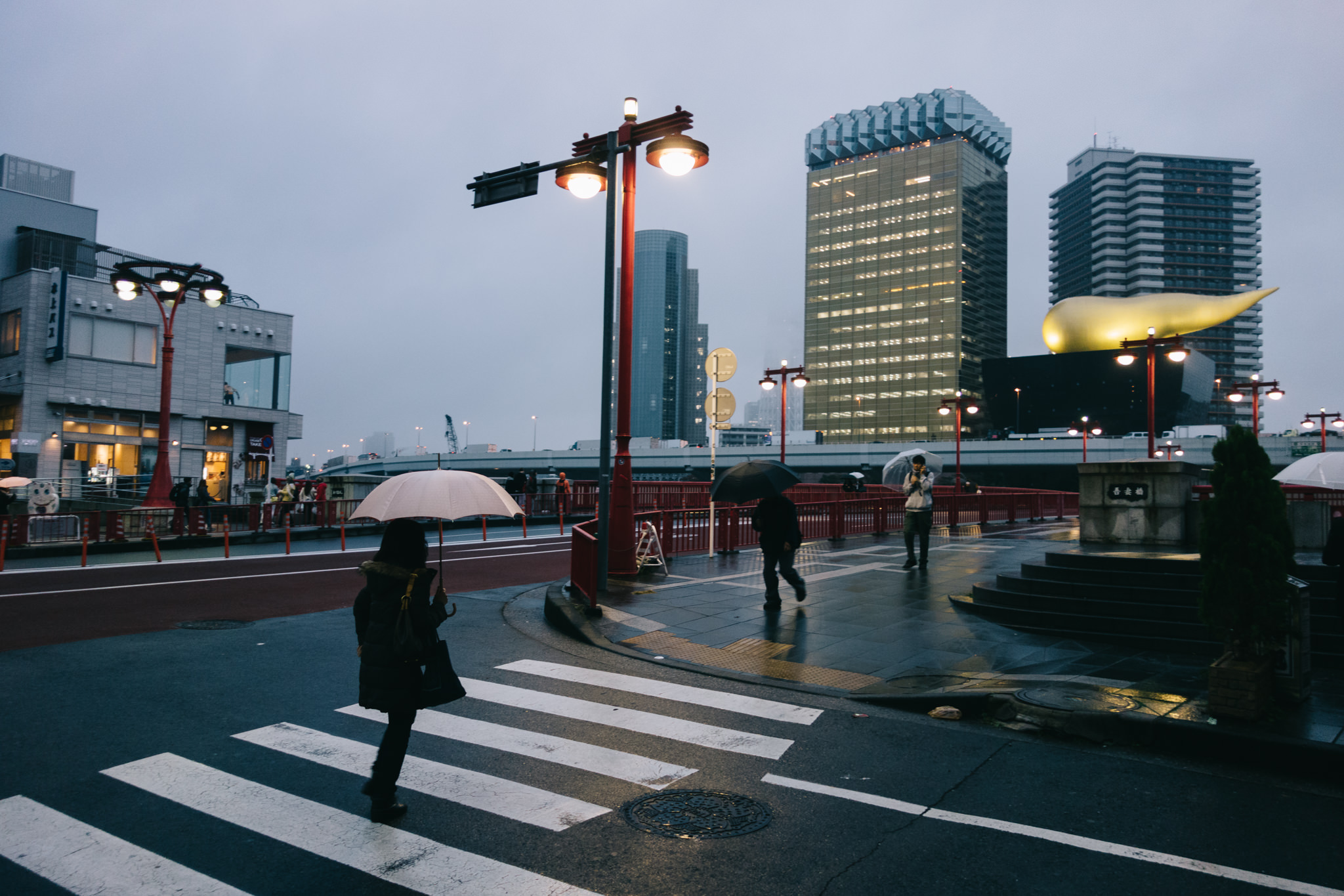 Person with umbrella crossing a street in Tokyo, Japan, with modern buildings in the background.