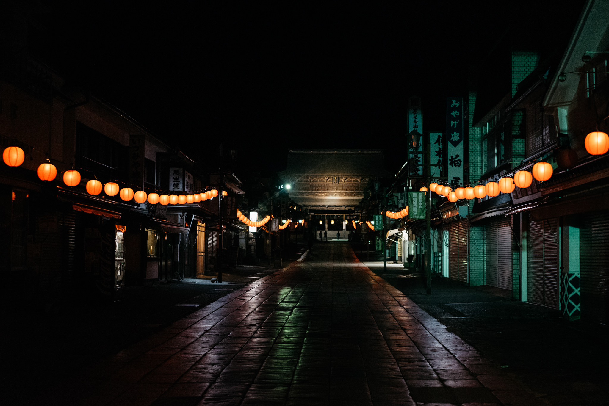 Night view of a Nagano street with orange lanterns leading to a temple.