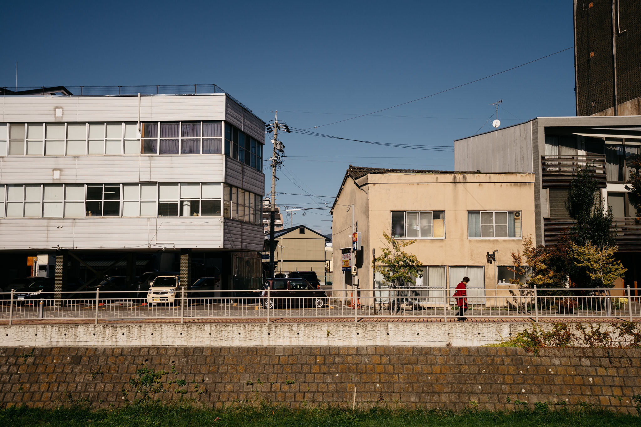 Person walking along a river in Matsumoto, Japan, between buildings.