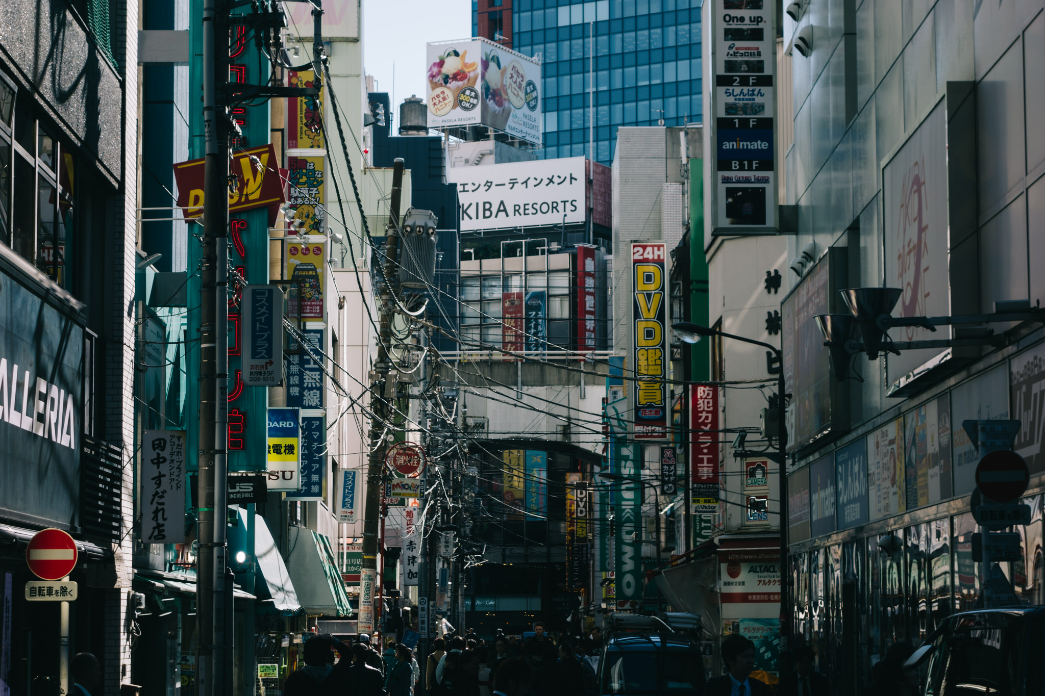 A narrow Tokyo street filled with vibrant signs and tangled wires.