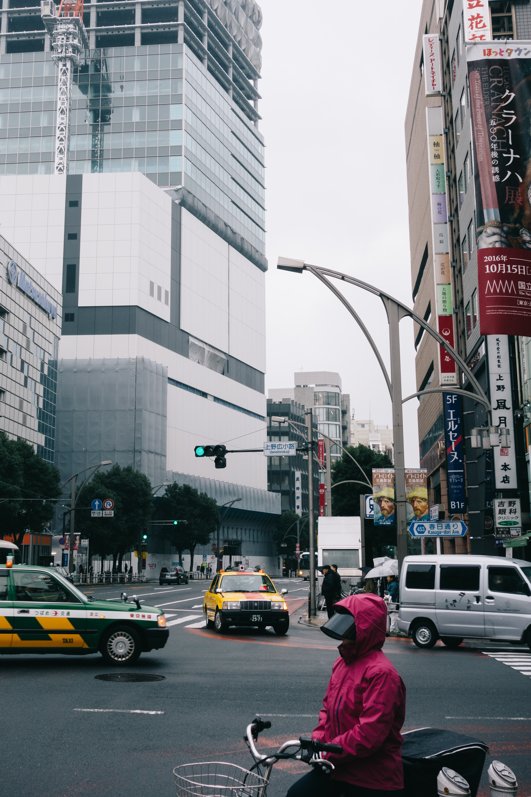 Tokyo street scene with a person on a bicycle, taxis, and a building under construction.