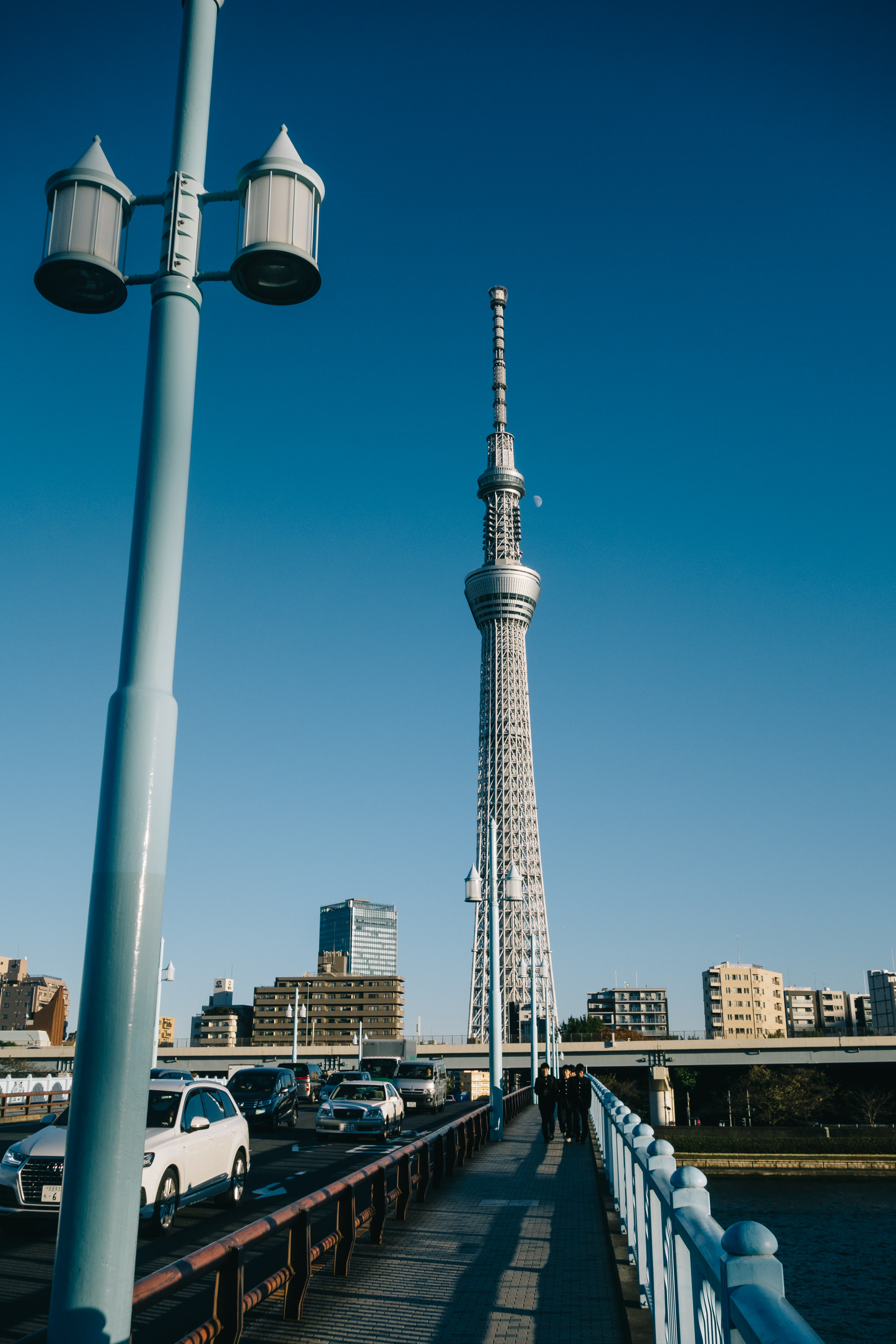 Tokyo Skytree viewed from a bridge with cars and pedestrians.