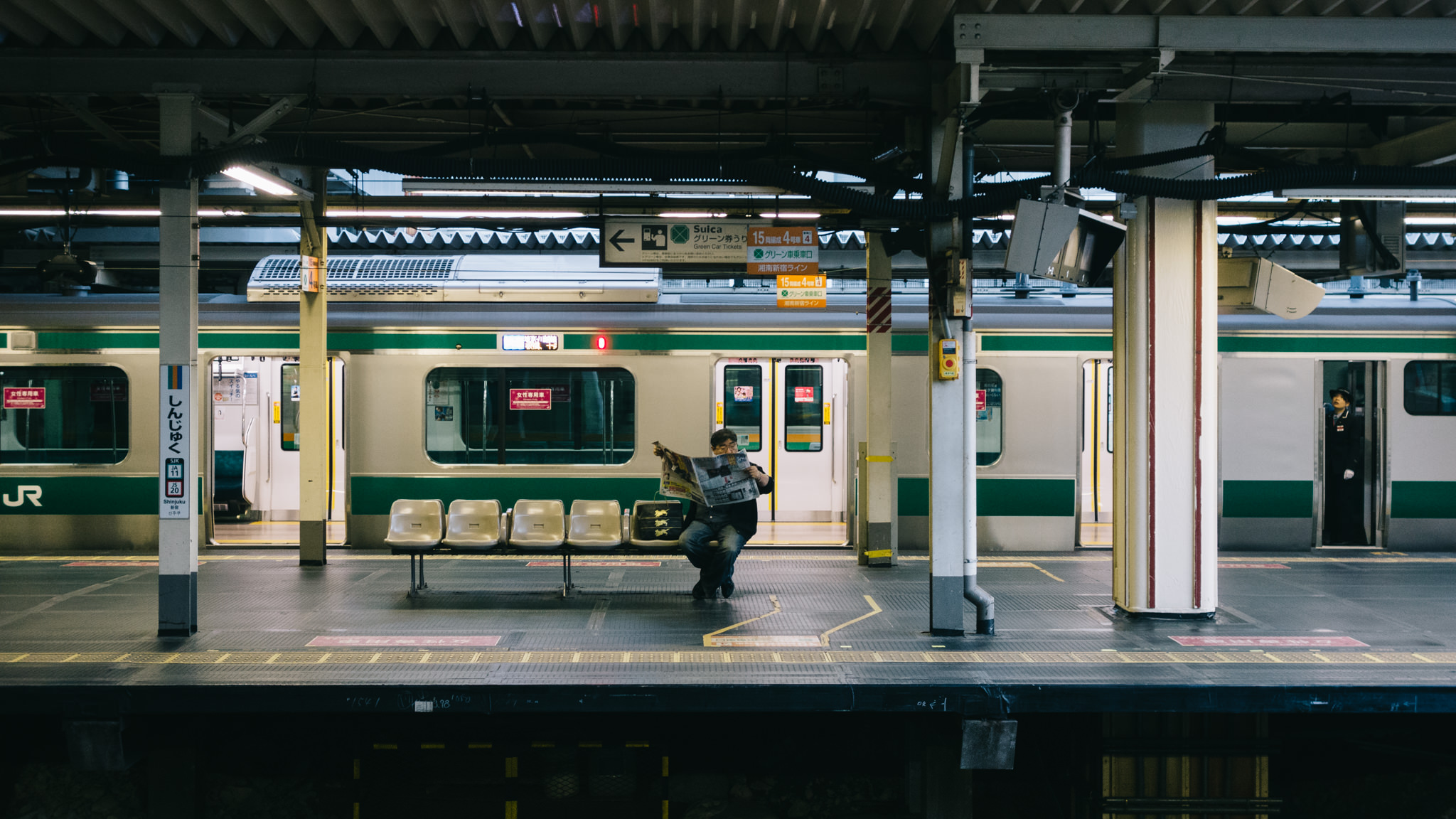 Man reading newspaper on bench at Tokyo train station.