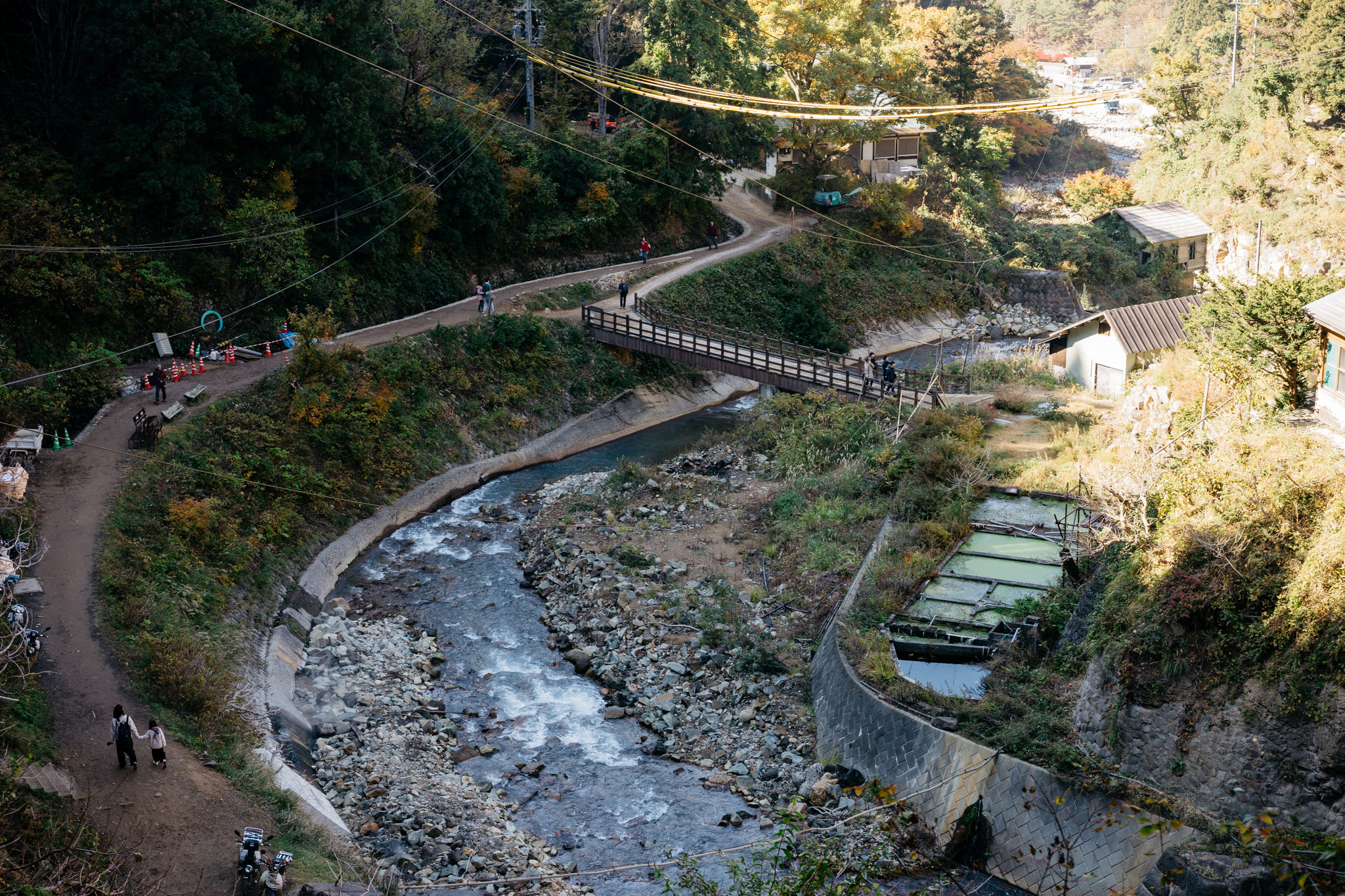 Aerial view of a valley with a river, footpaths, a bridge, and small buildings.