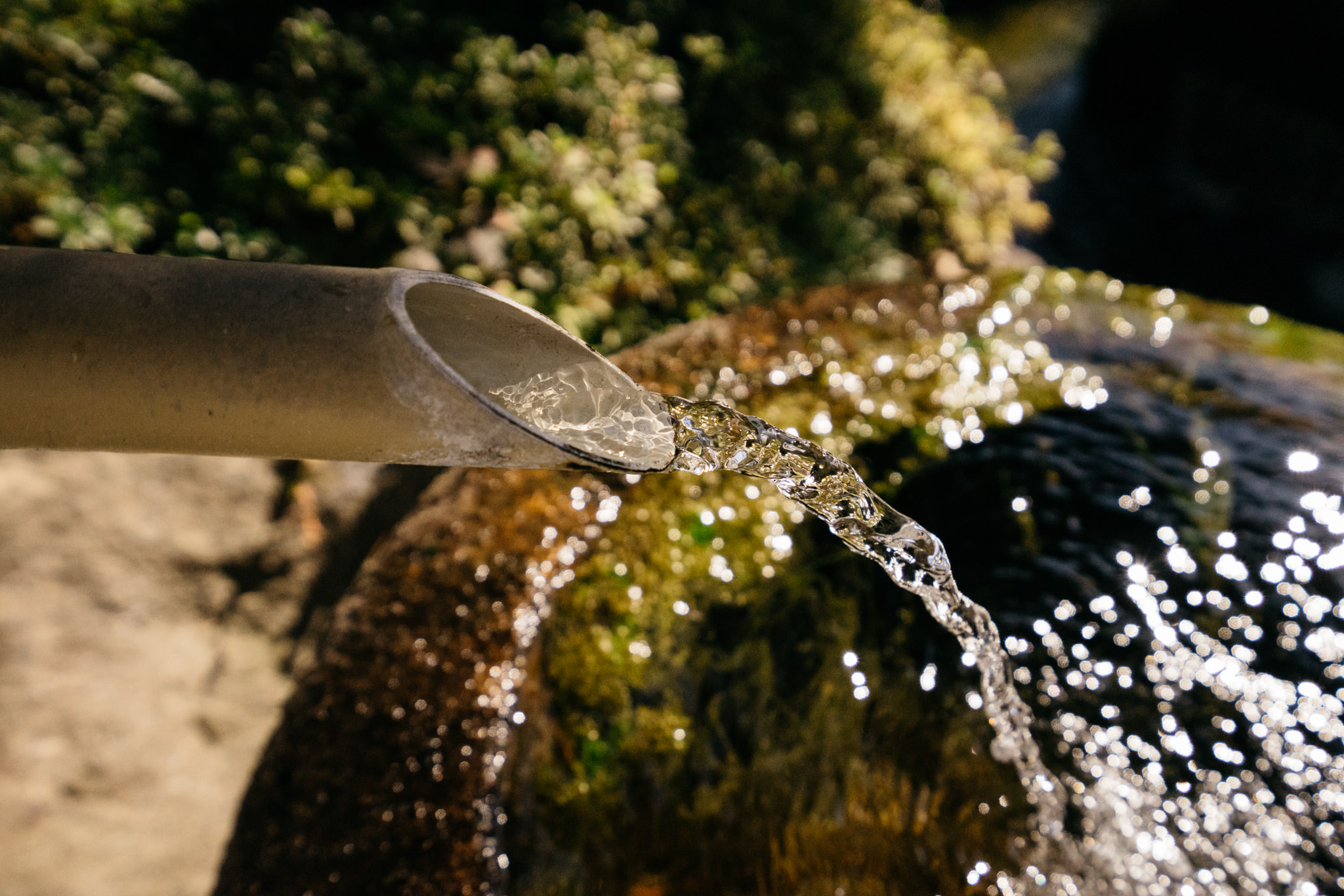 Water flowing from a bamboo pipe into a stone basin.