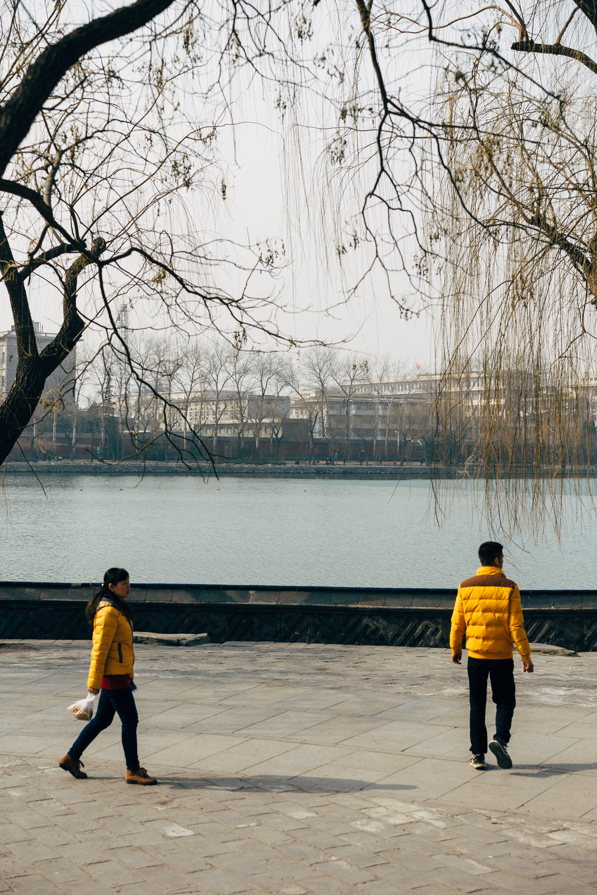 Two people in yellow jackets walking by a lake in Beihai Park, Beijing.