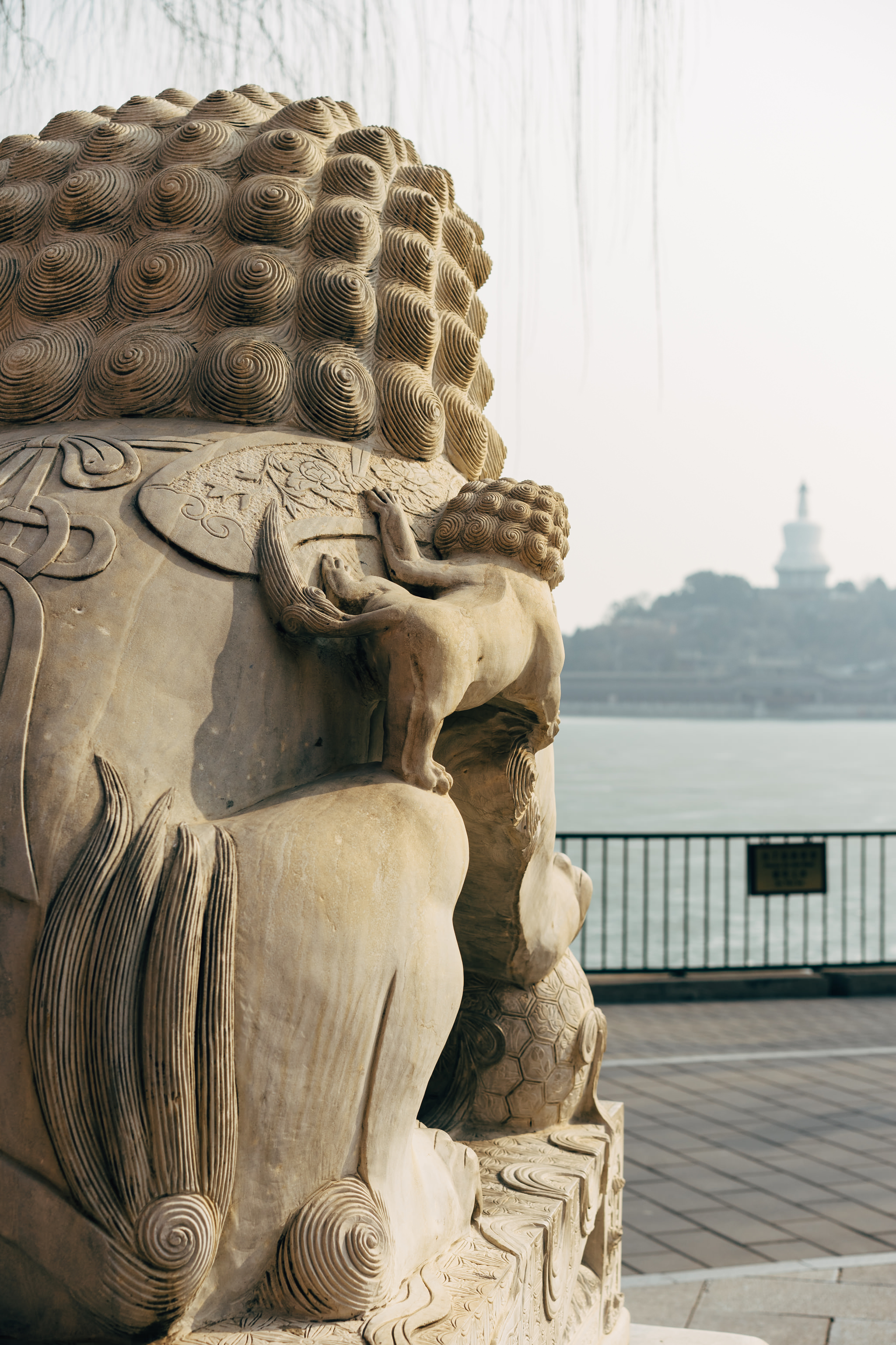 Close-up of an intricately carved stone lion statue in Beihai Park, Beijing, with a pagoda visible in the blurred background.