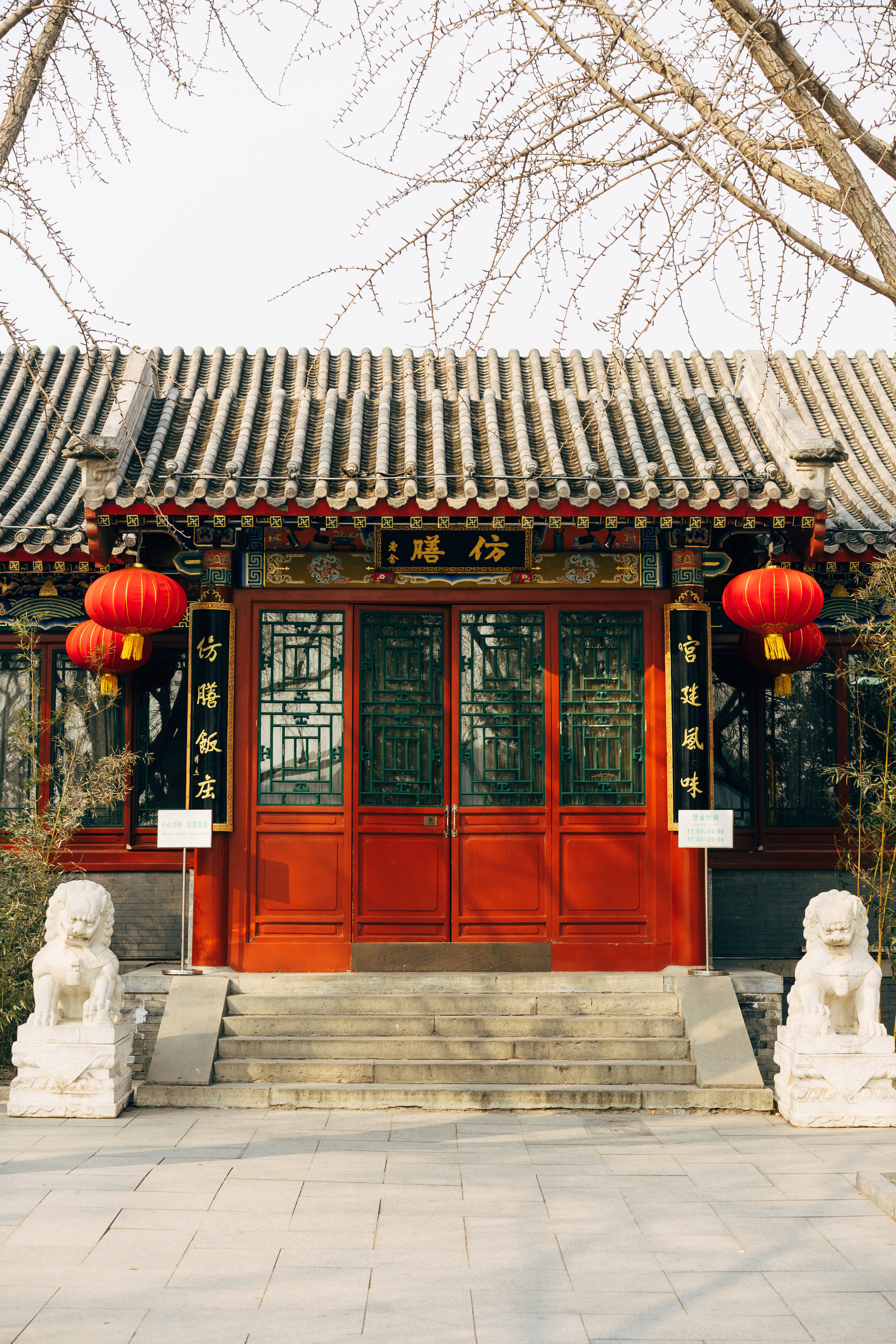 Red building entrance in Beihai Park, Beijing, with stone lion statues and red lanterns.