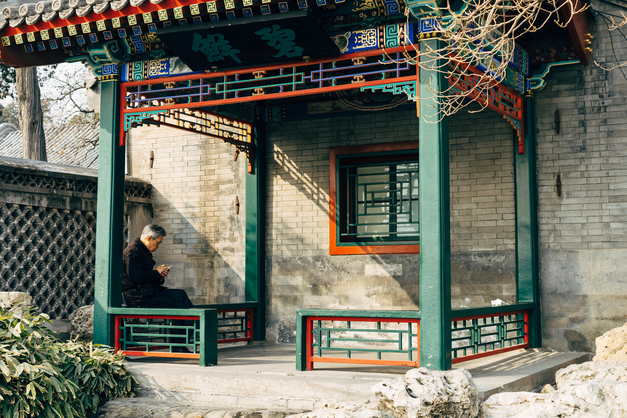 Elderly man using phone in ornate Beihai Park pavilion.
