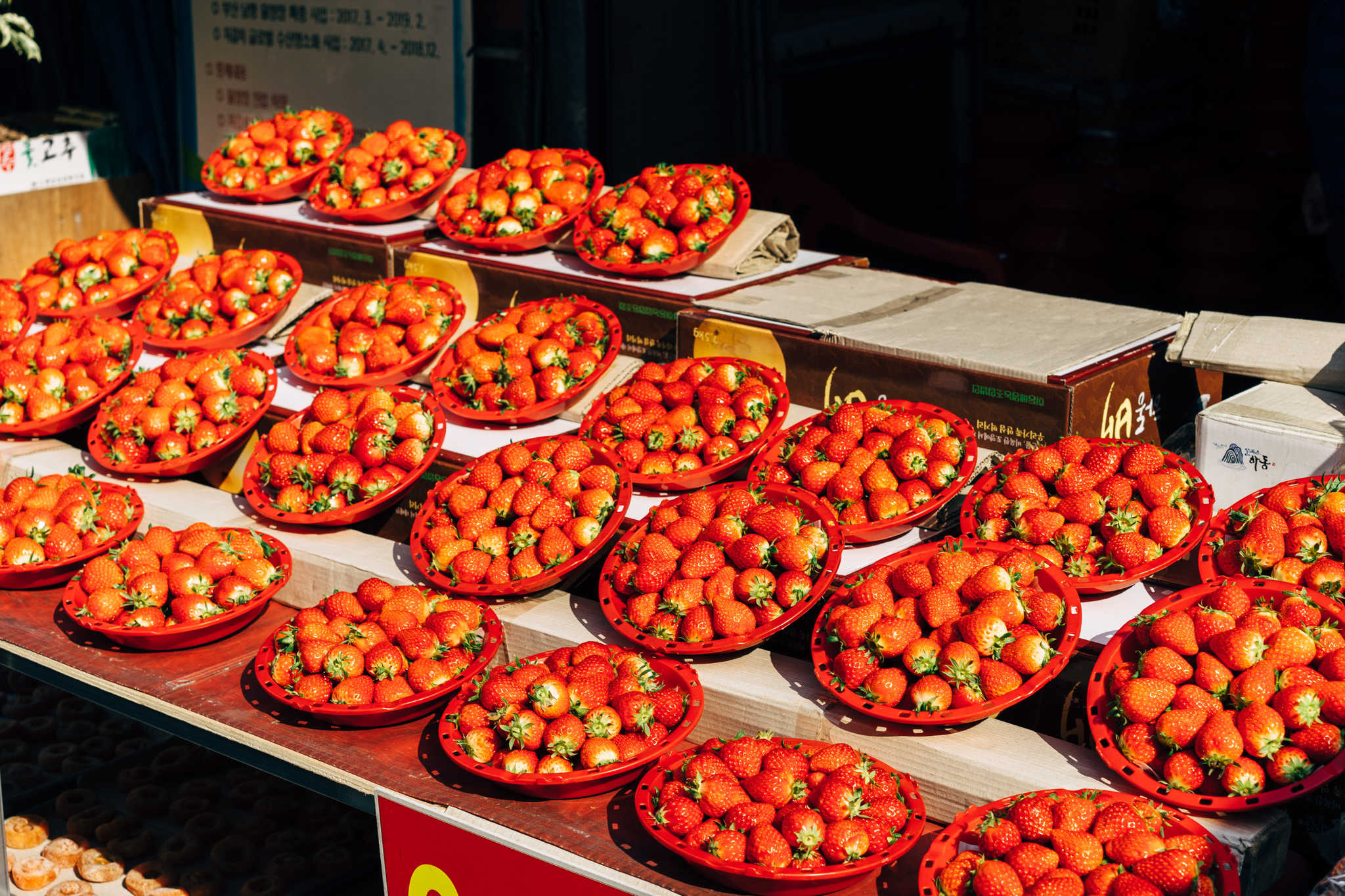 Busan market stall displaying numerous red plastic baskets overflowing with fresh strawberries.