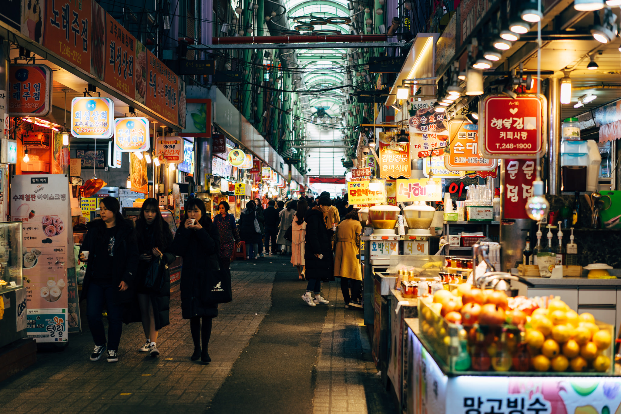 Busy indoor Busan market hallway with food stalls and shoppers.