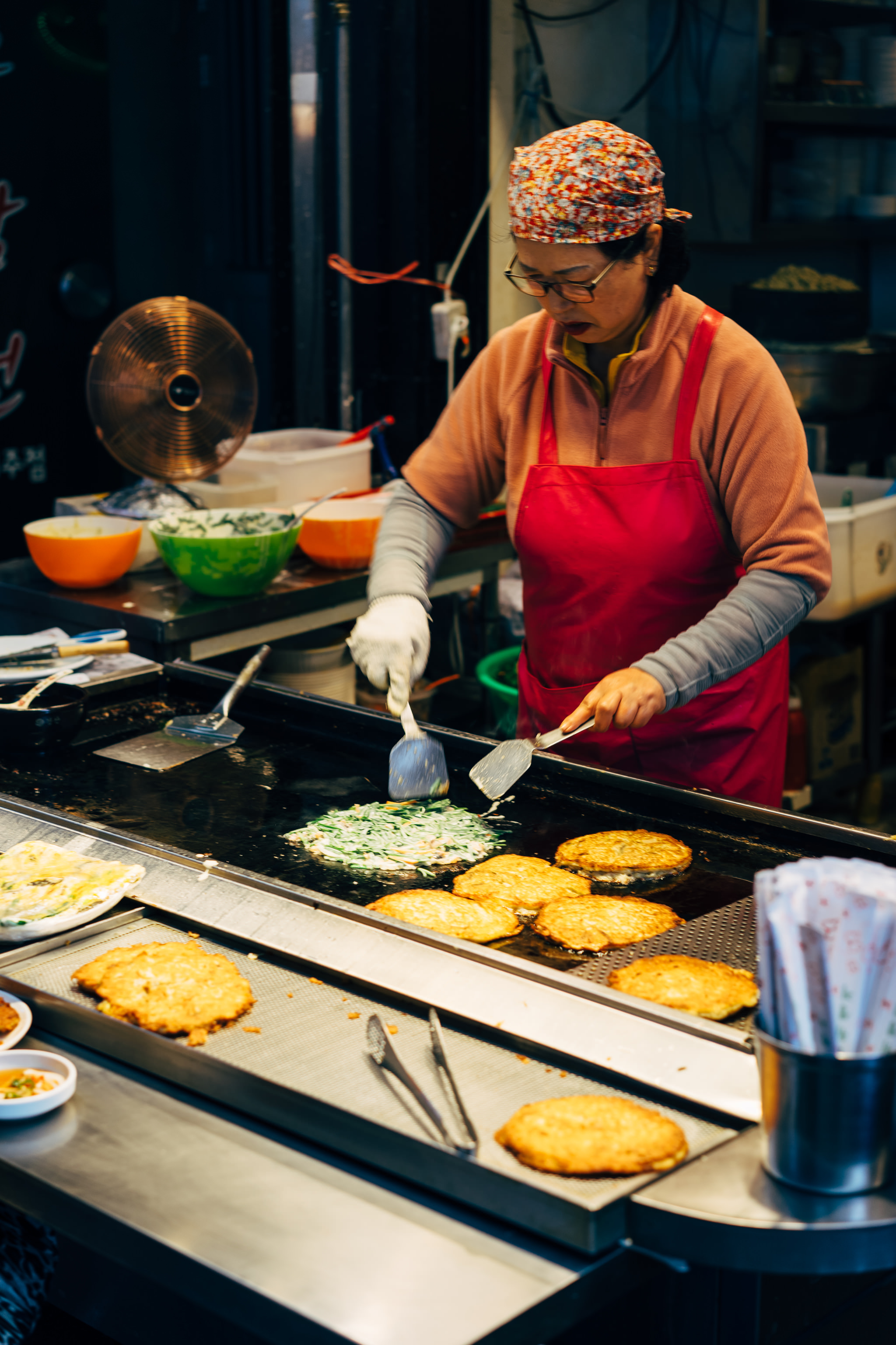 Woman cooking pancakes on a griddle at a Busan market.