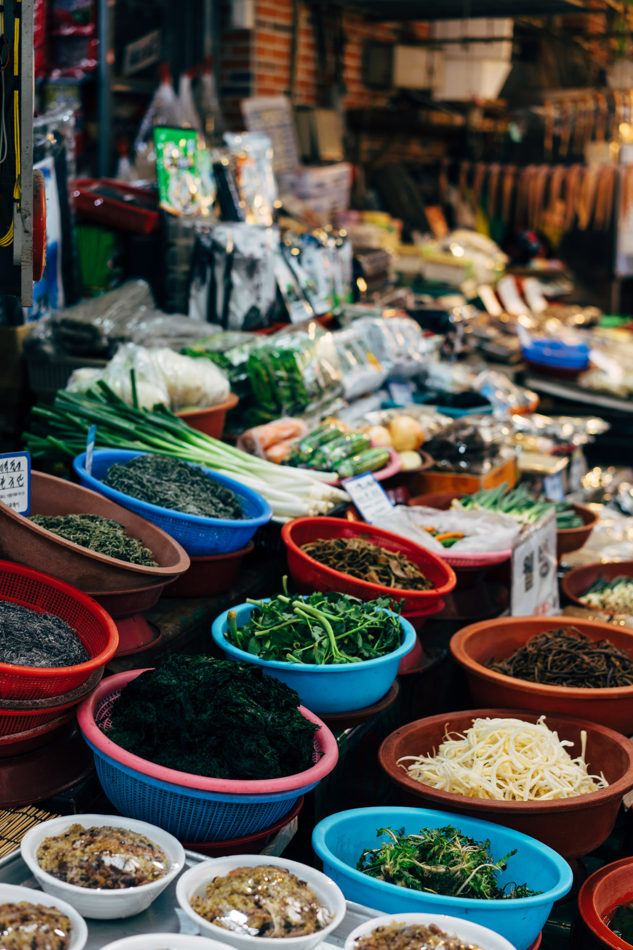 Busan market stall overflowing with colorful bowls of various vegetables and seaweed.