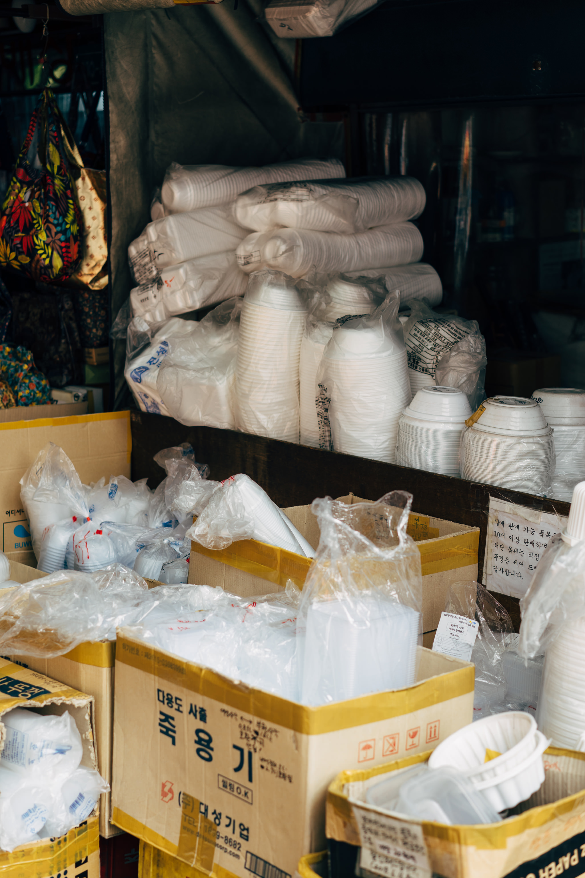 Stacks of plastic cups and containers in cardboard boxes at a Busan market.