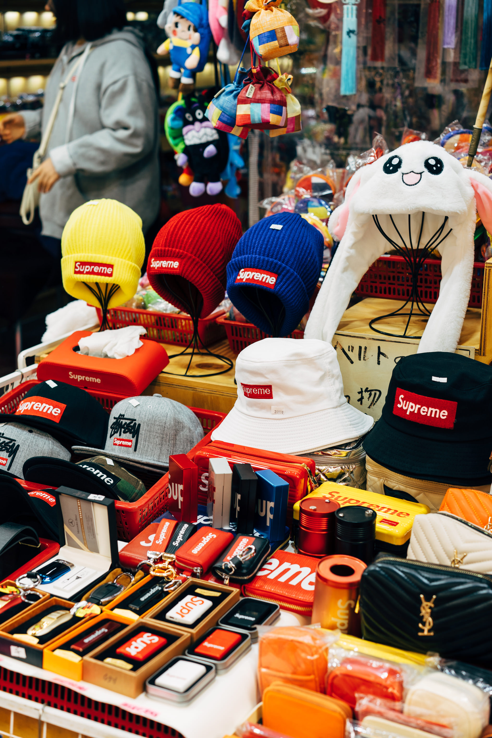 Busan market stall displaying various Supreme-branded hats, bucket hats, and accessories.