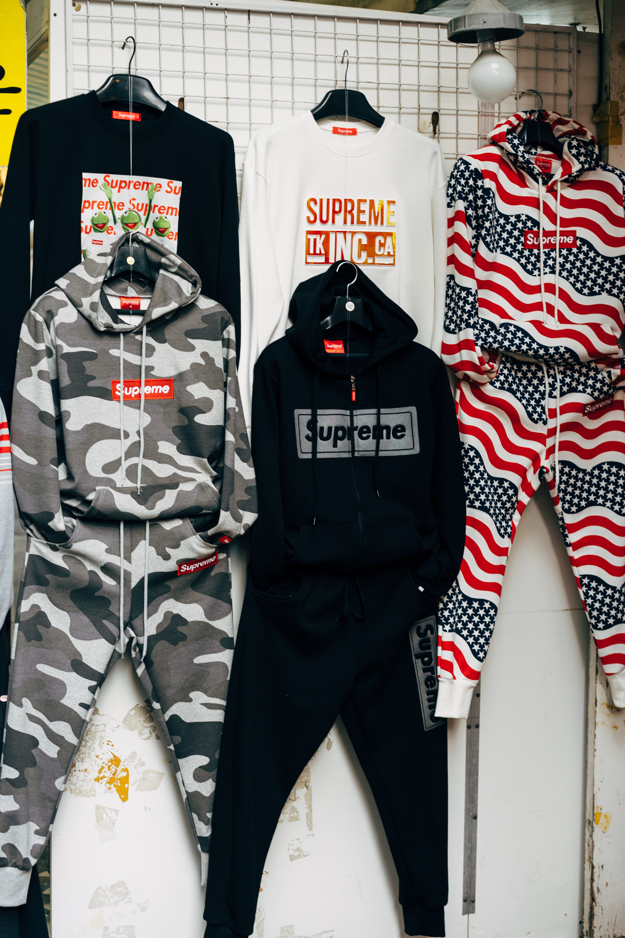 Several Supreme-branded hoodies and sweatpants hanging on a rack.