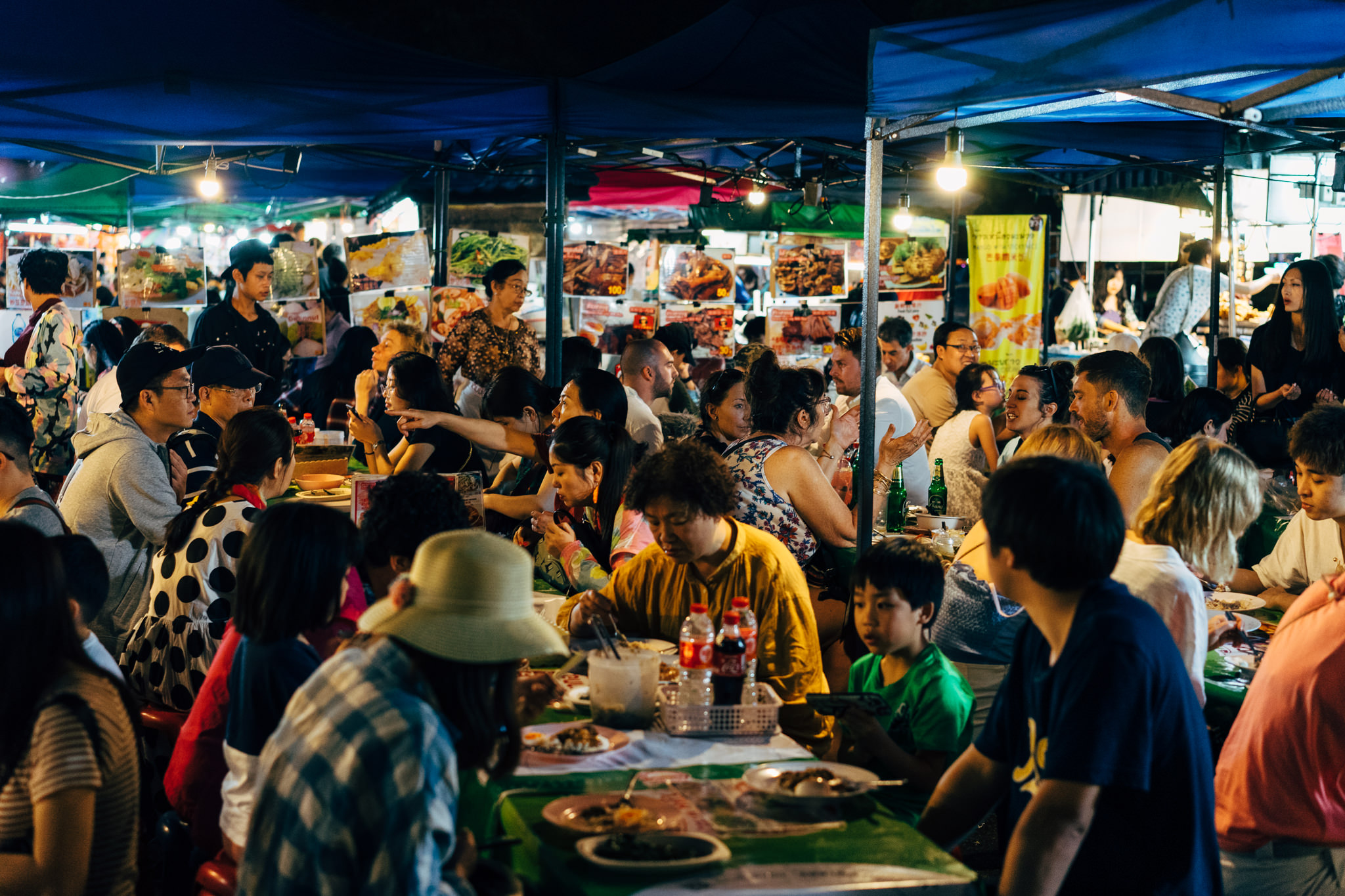 Crowded Chiang Mai night market with people eating at tables under tents.