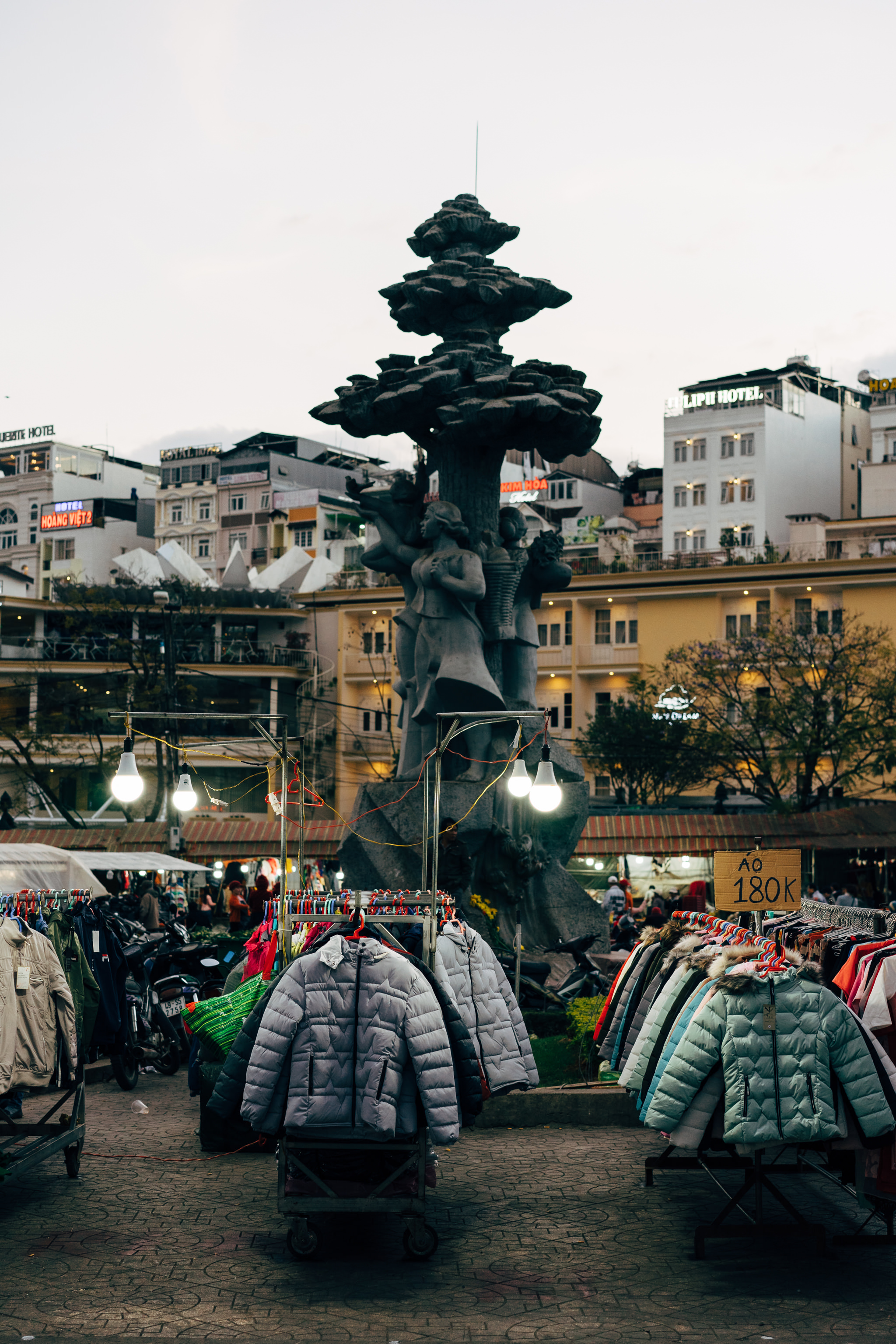 Da Lat market scene with clothing racks and a tree statue.