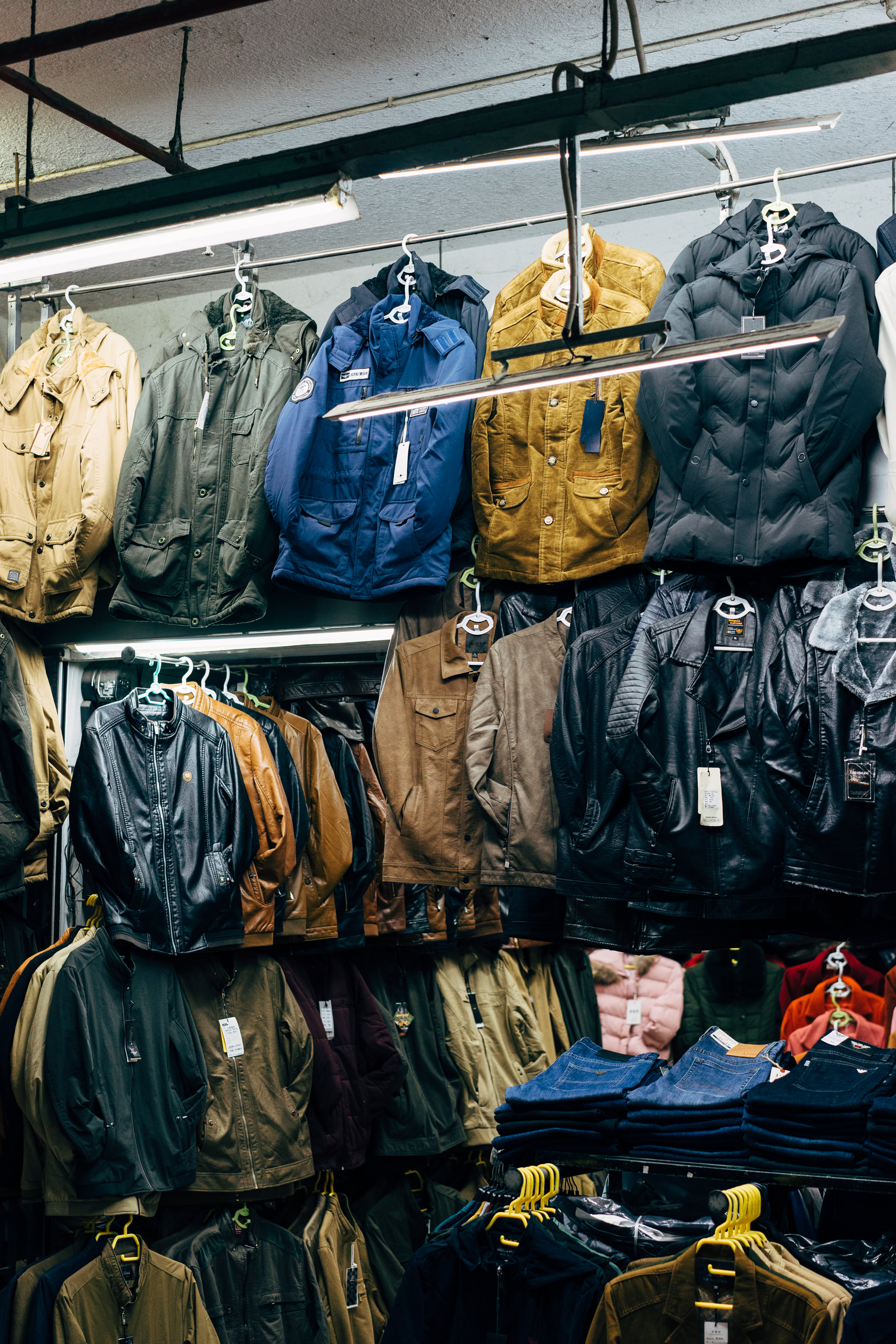 Many jackets and jeans hanging on racks in a market.